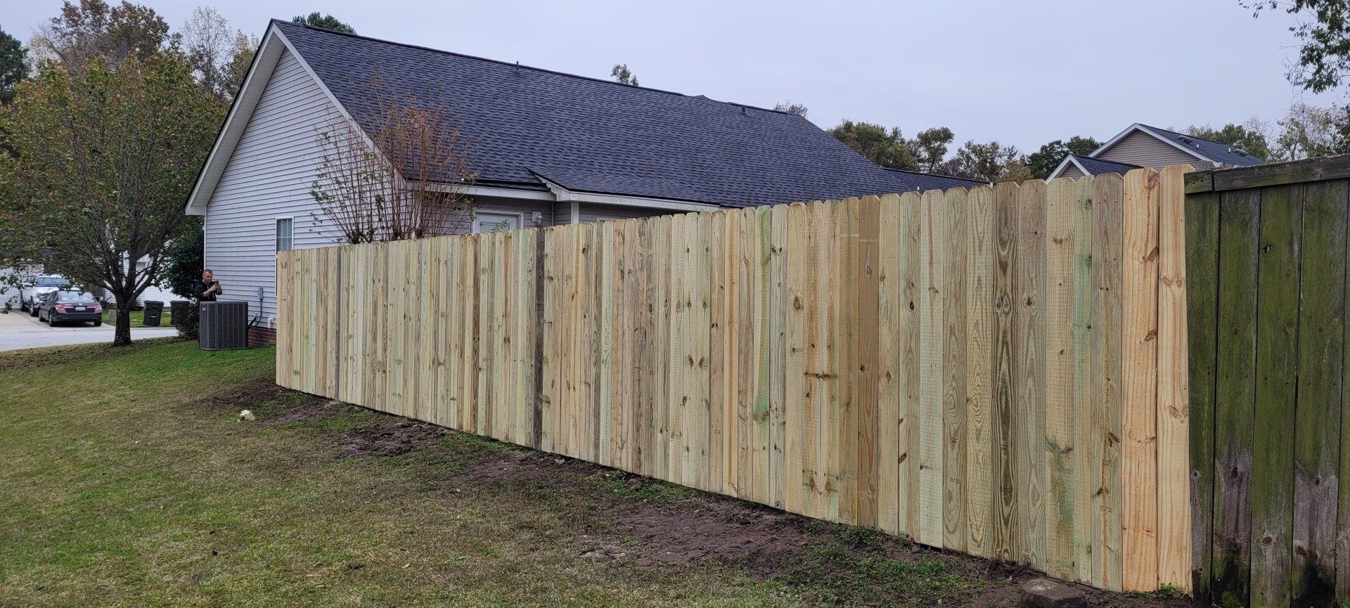 A wooden fence next to a house with a dark roof and a lawn.