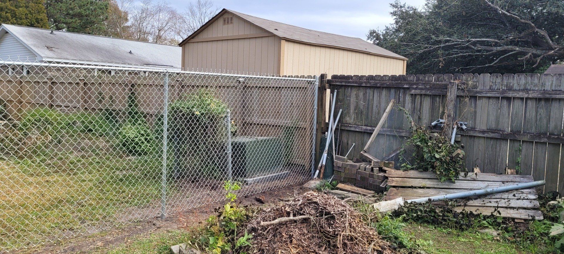 A chain-link fence and wooden fence enclose a backyard with a shed. Debris and foliage are scattered nearby.