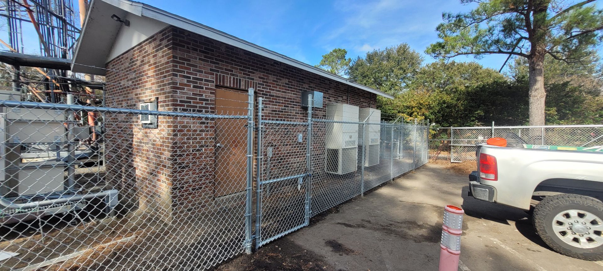 A brick building with air conditioning units along a fenced perimeter. A pickup truck is parked nearby.