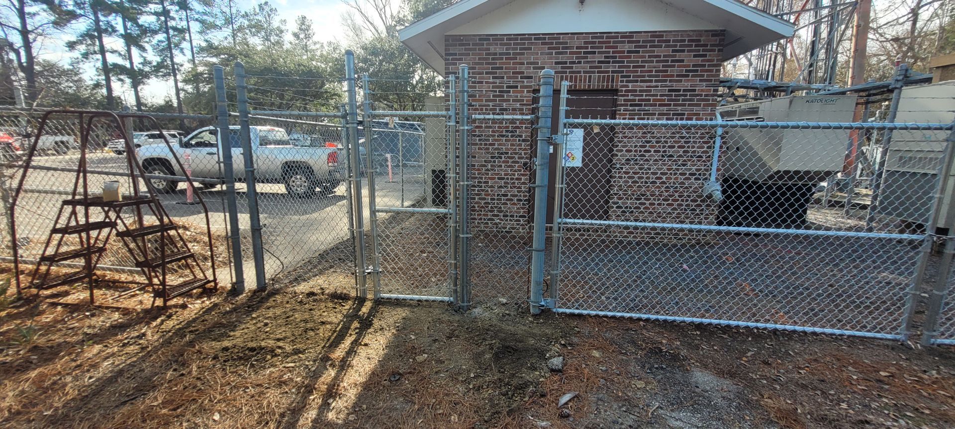 A chain link fence surrounds a brick building. A truck and trees are visible in the background.