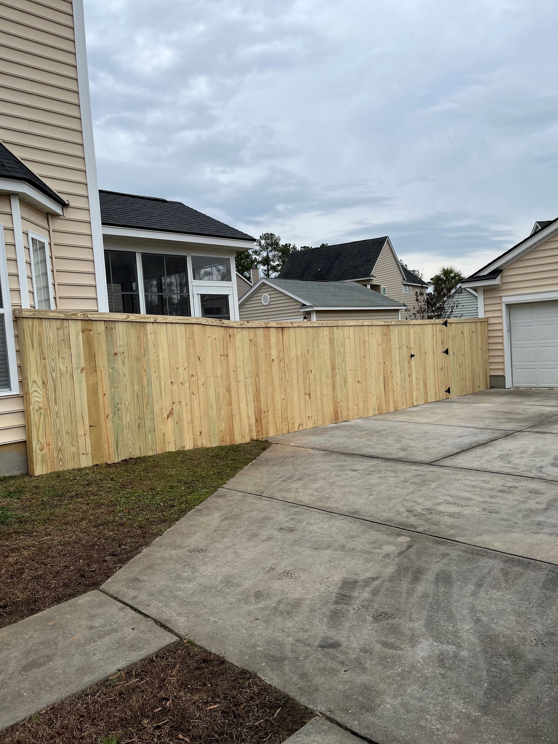 Wooden fence along a house and driveway; cloudy day.