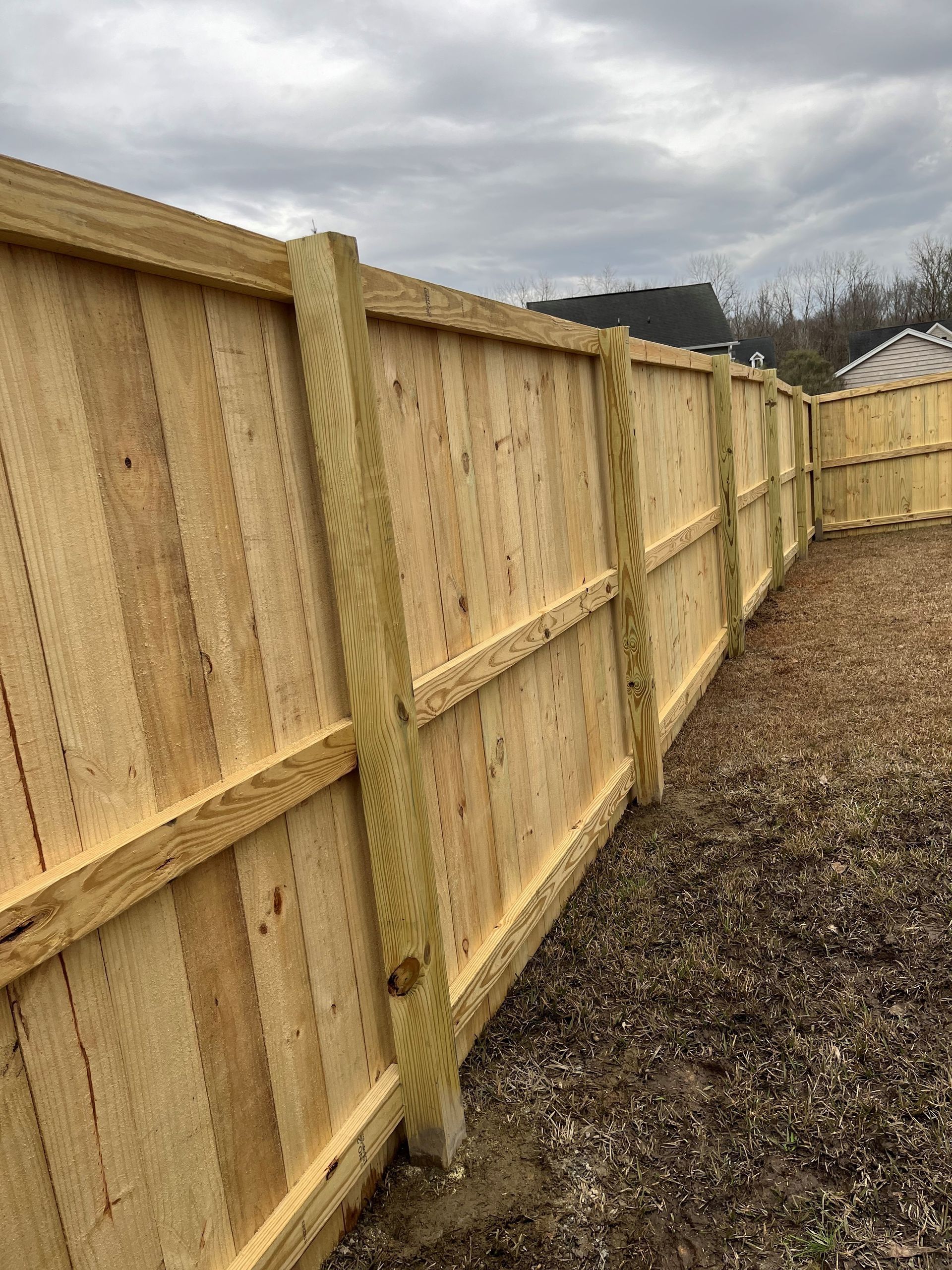 Wooden fence in a yard with gravel ground and cloudy sky.