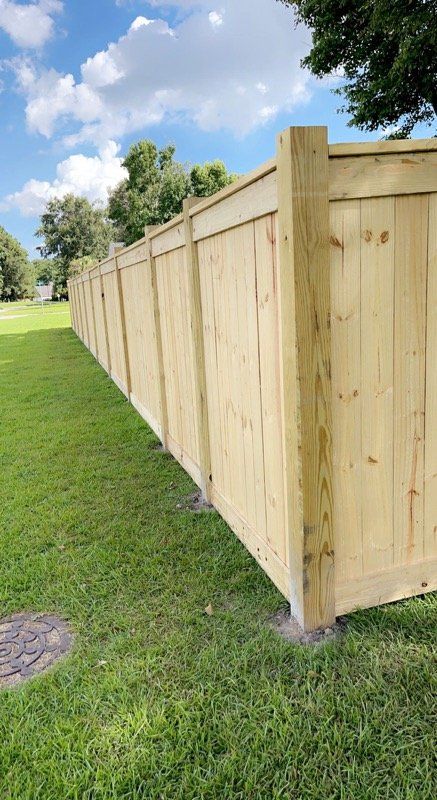 Wooden privacy fence on a grassy lawn under a blue sky with clouds.