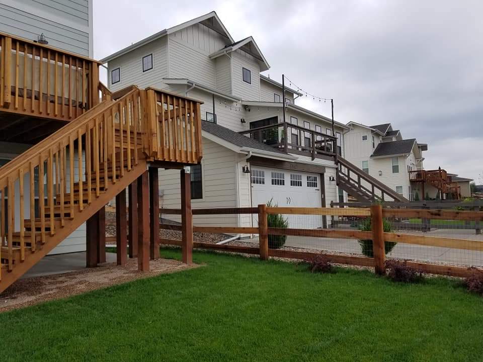 Wooden deck and stairs on a white house, overlooking a grassy yard and wooden fence, under a cloudy sky.