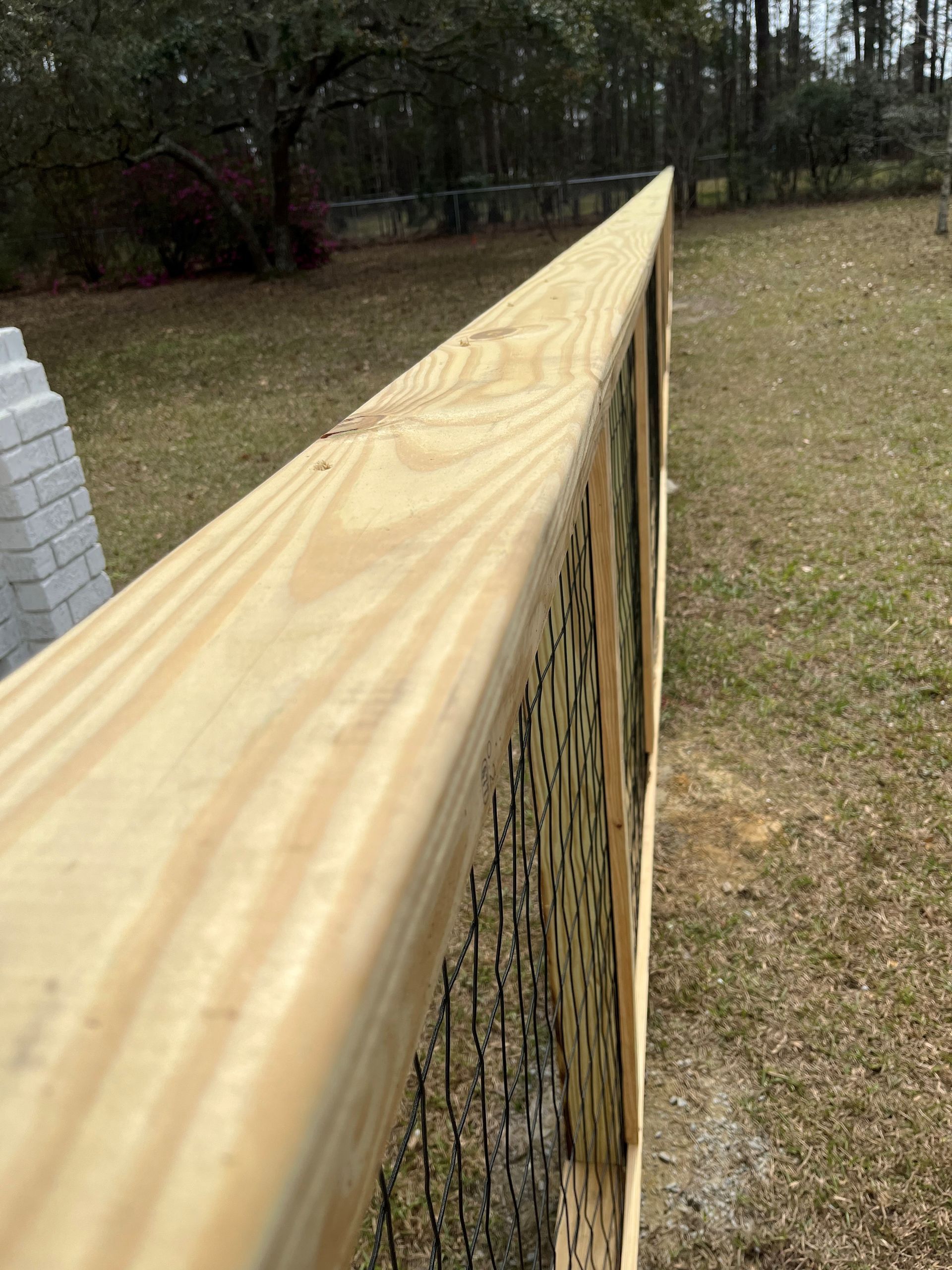 Close-up of a new wooden fence with latticework and a grassy backyard.