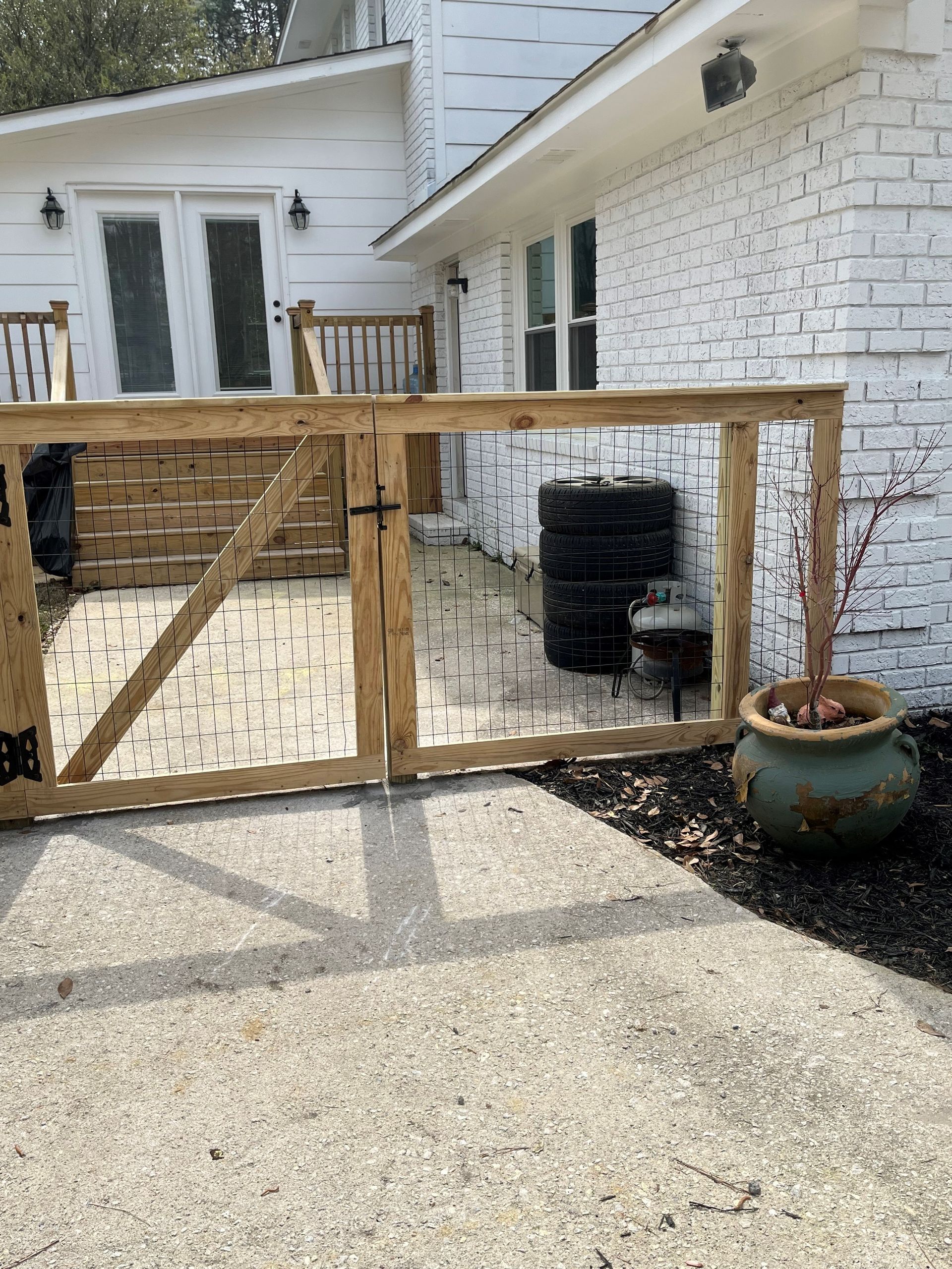 Wooden gate encloses a brick patio area adjacent to a white brick house.  A large potted plant sits nearby.