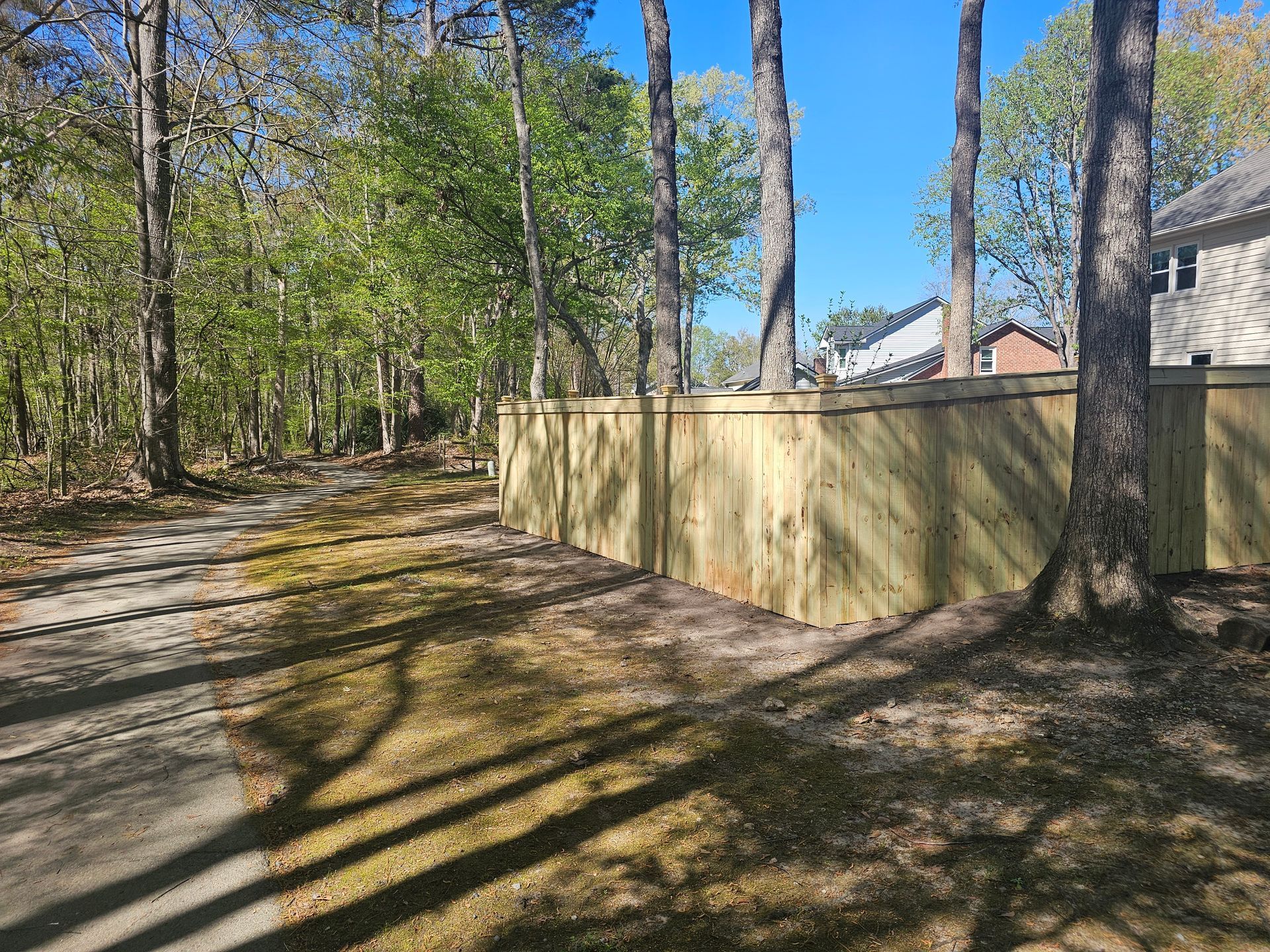 Wooden fence bordering a wooded area with trees and a house in the background on a sunny day.