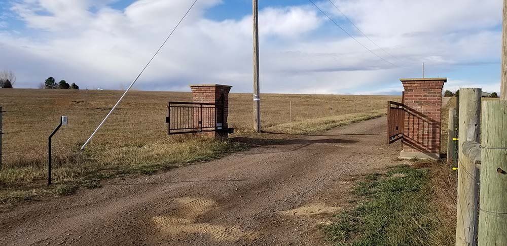 Open gate on a dirt road leading to a field under a cloudy sky.