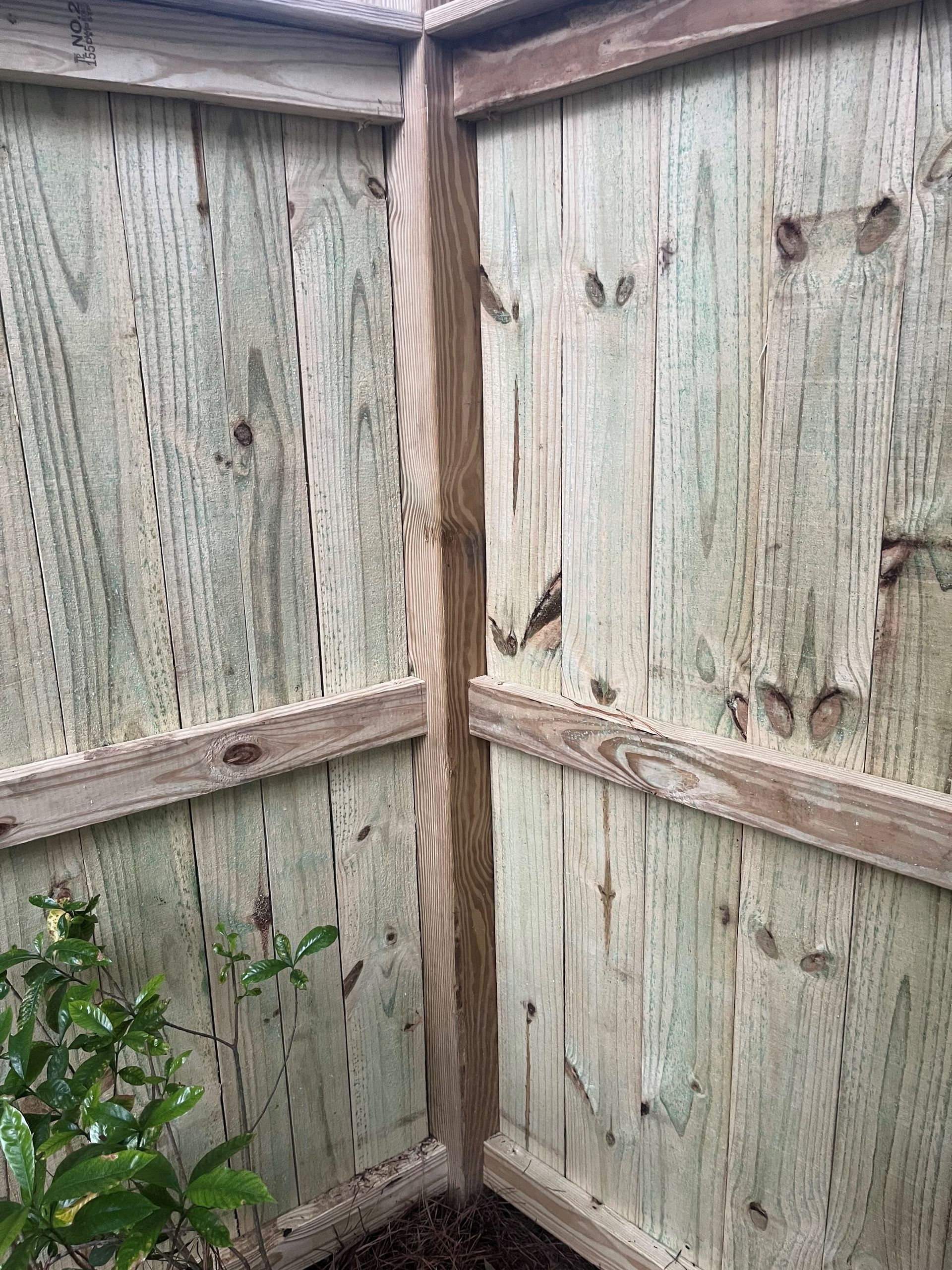 Corner of a wooden fence, with vertical planks and horizontal supports, in a natural setting.