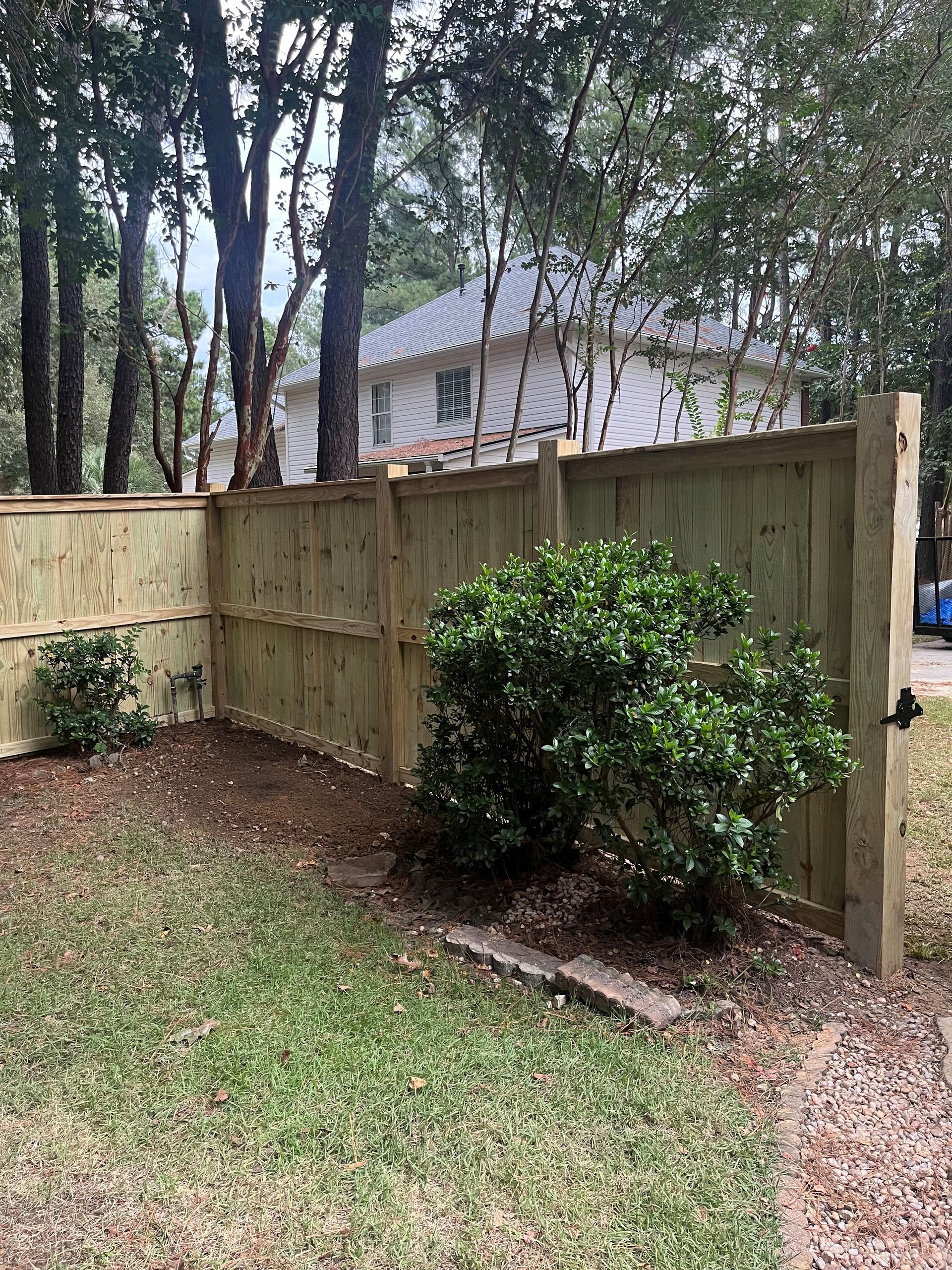 Wooden fence with small shrubs and grass in front. House in the background.