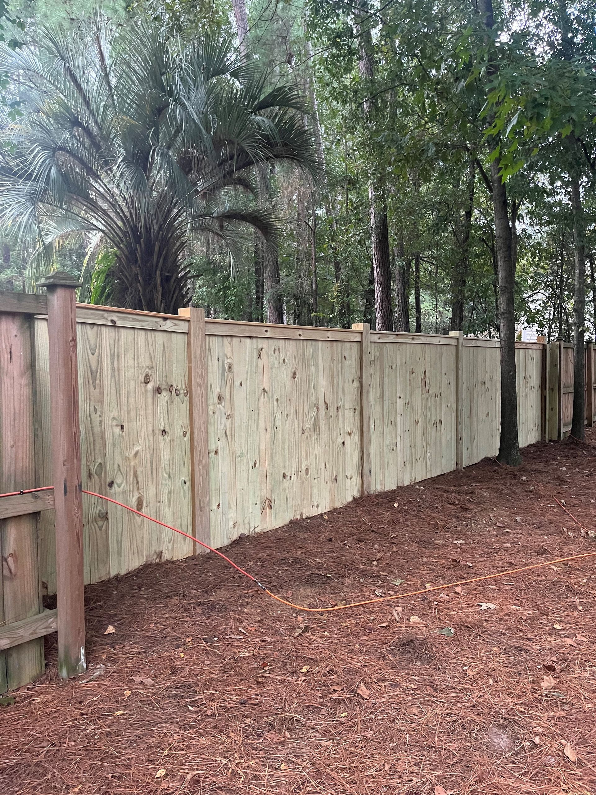 Wooden fence in a yard with mulch. Trees are in the background.
