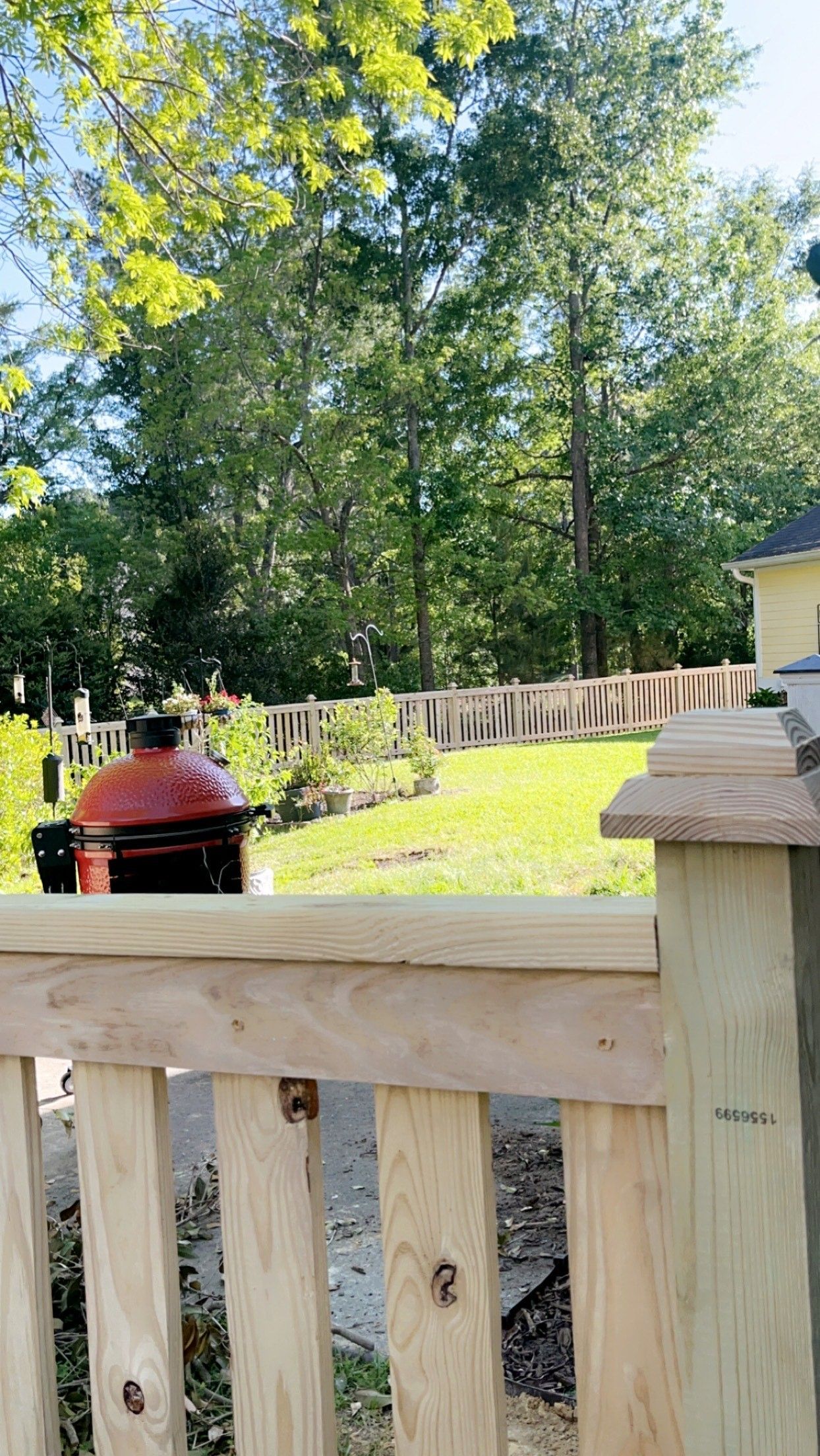 Wooden fence in focus; background features grassy yard, trees, and red grill.