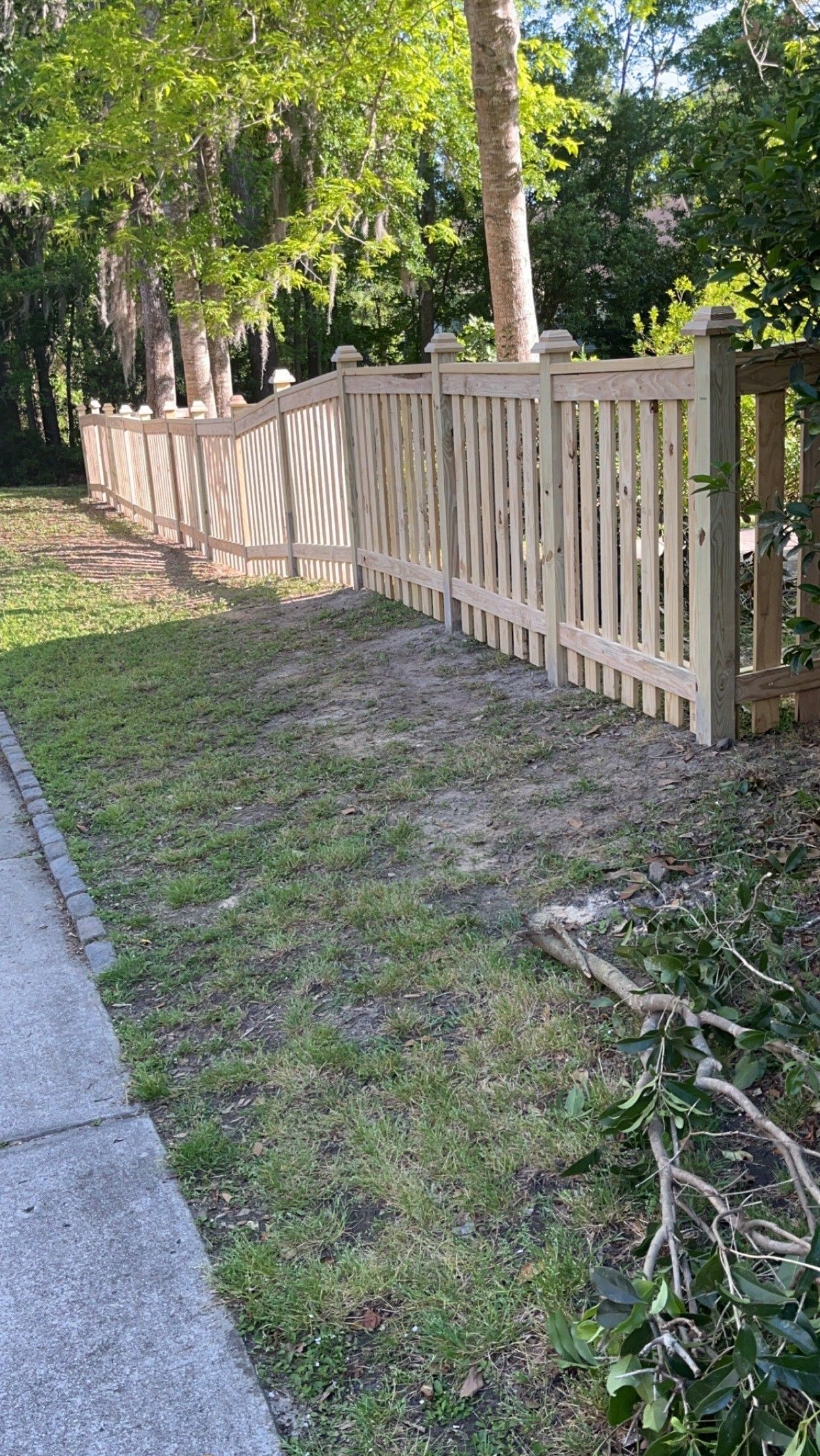 Wooden picket fence along a grassy area next to a sidewalk.