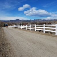 Dirt road with white fence, blue sky, and distant mountains.