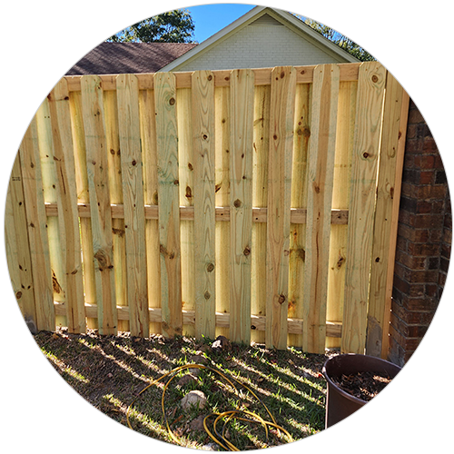 Wooden fence against a brick wall, with a partial view of a house and blue sky.