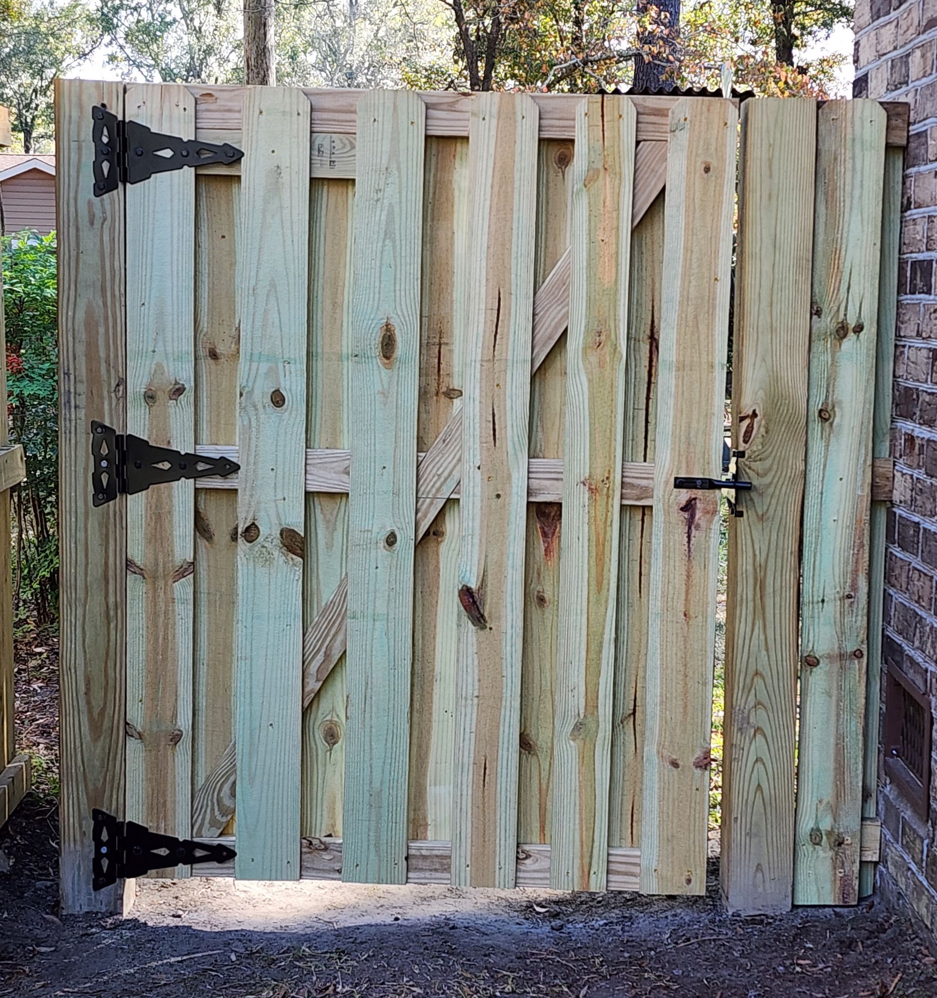 Wooden fence gate with black hinges and latch, unpainted wood.