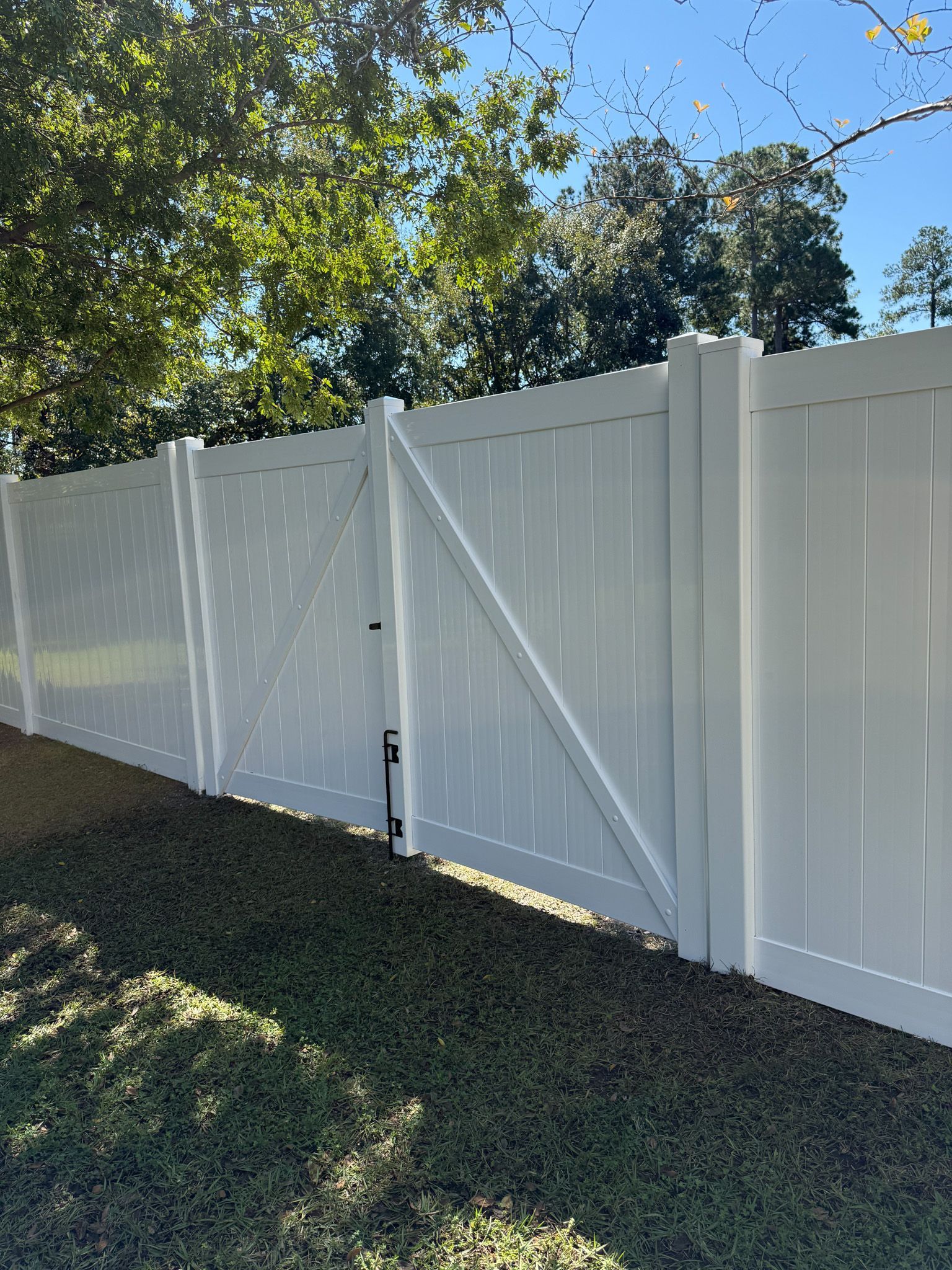 White vinyl fence with gate, set against a green lawn and trees under a blue sky.