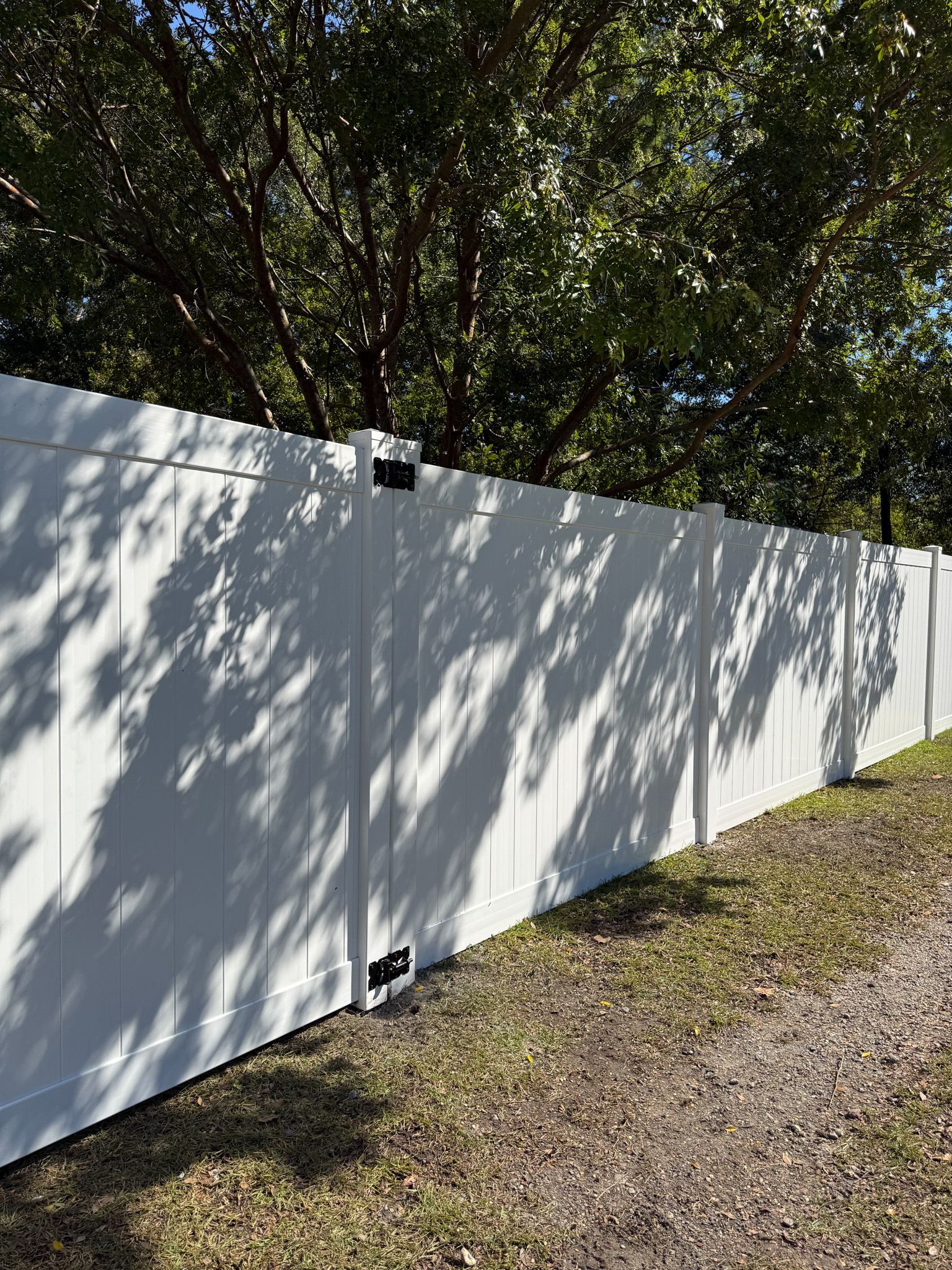 White vinyl fence alongside a gravel path, with shadows cast by a tree above.