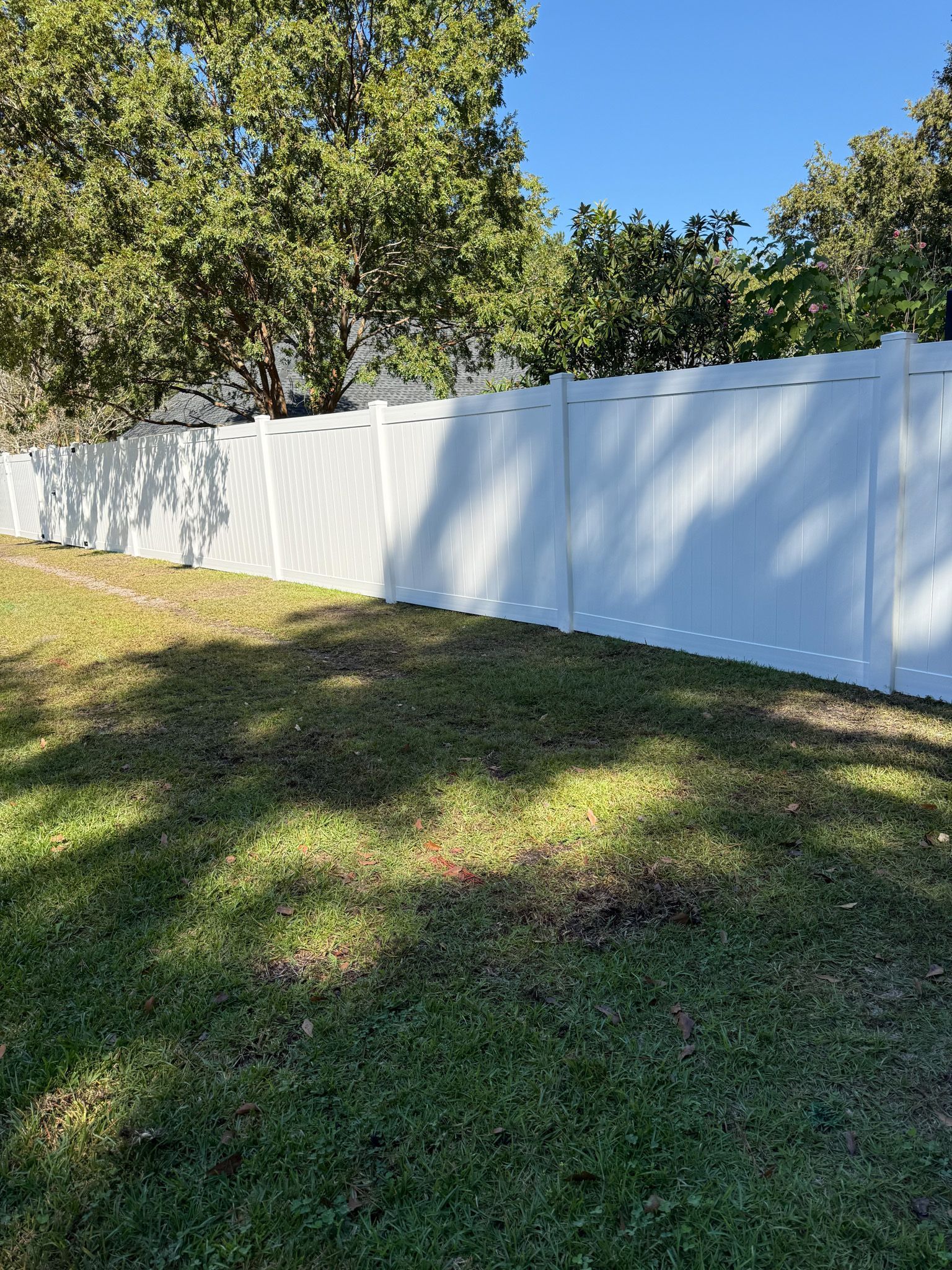 White vinyl fence in a grassy yard, trees in the background, sunny day.