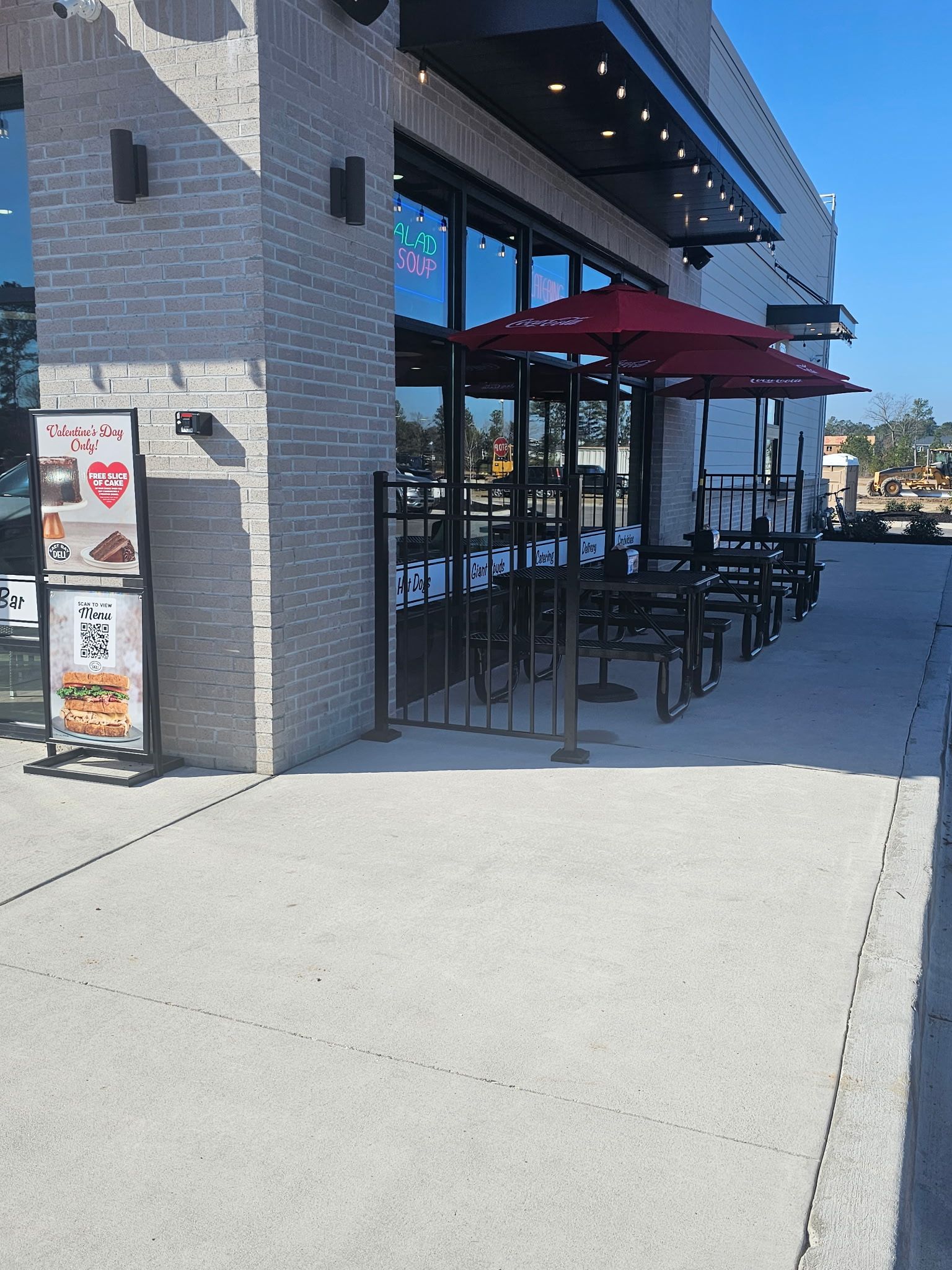 Exterior of restaurant with outdoor seating under red umbrellas; light brick facade, sign, and sidewalk.