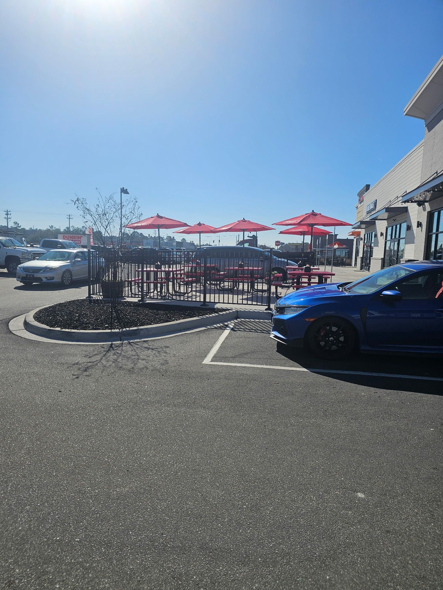 Outdoor seating area with red umbrellas and tables at a fast food restaurant; blue car in parking space.