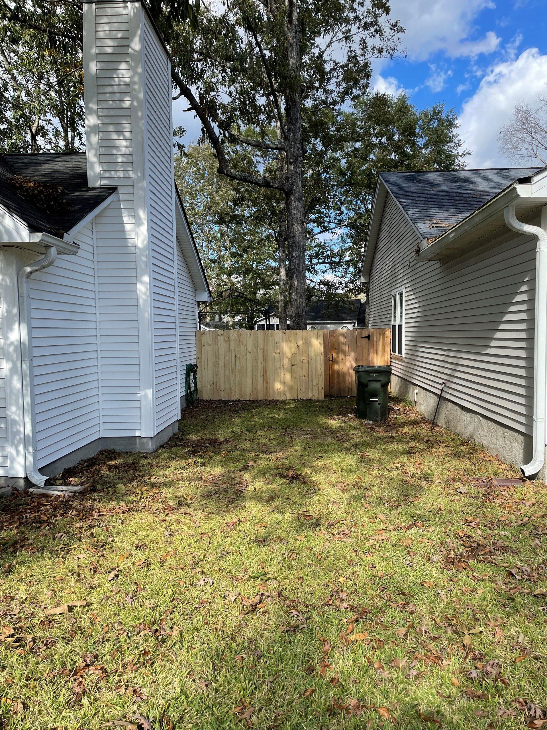 Backyard view with a wooden fence, buildings on either side, and green grass.