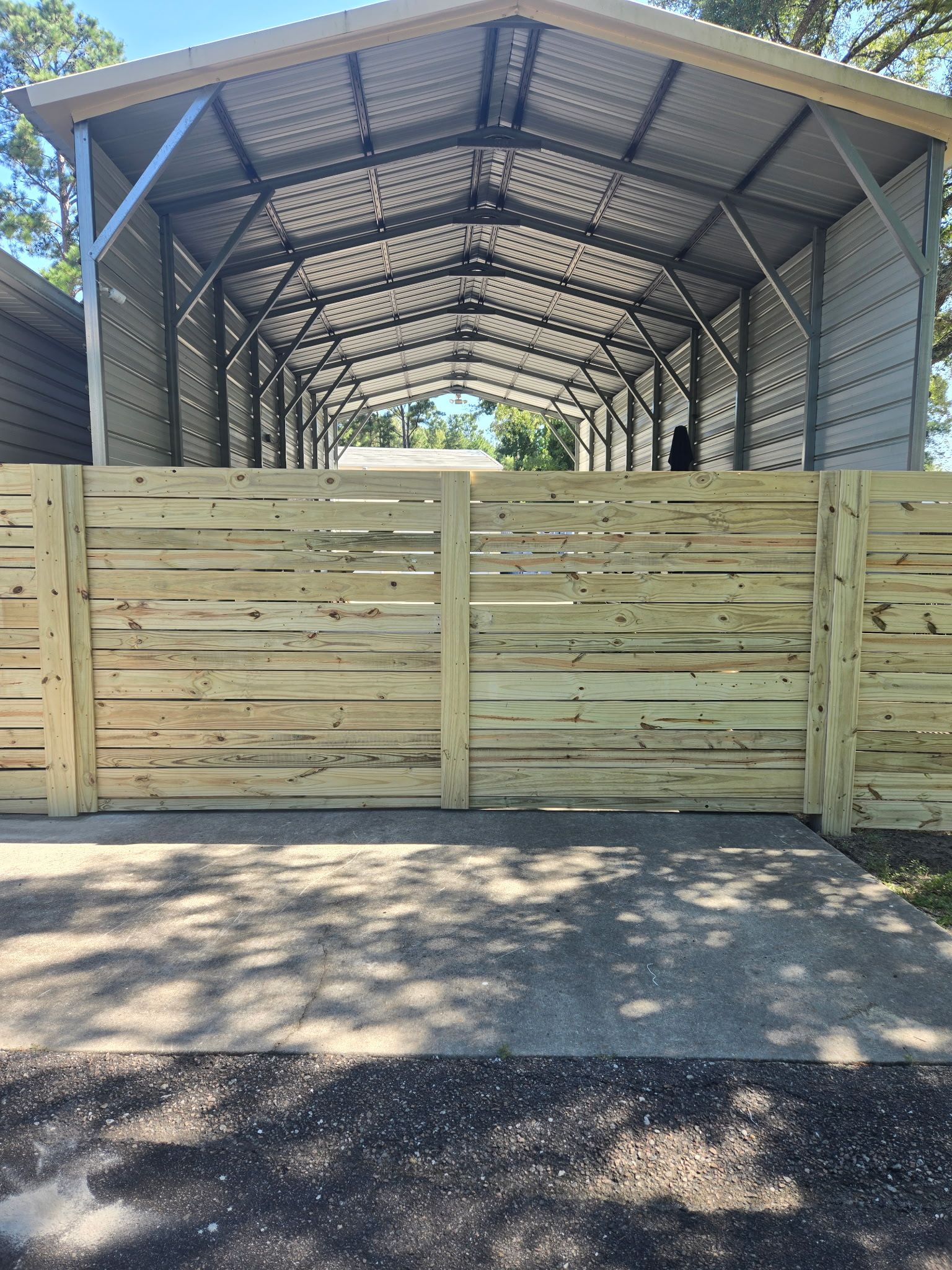 Wooden gate in front of a metal carport structure, set on a concrete driveway.