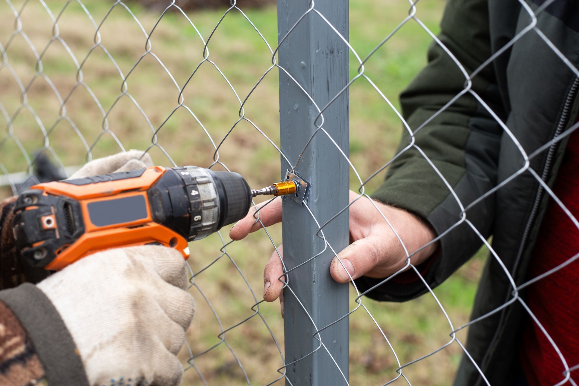 Person using a drill to secure wire mesh fence to a gray post.