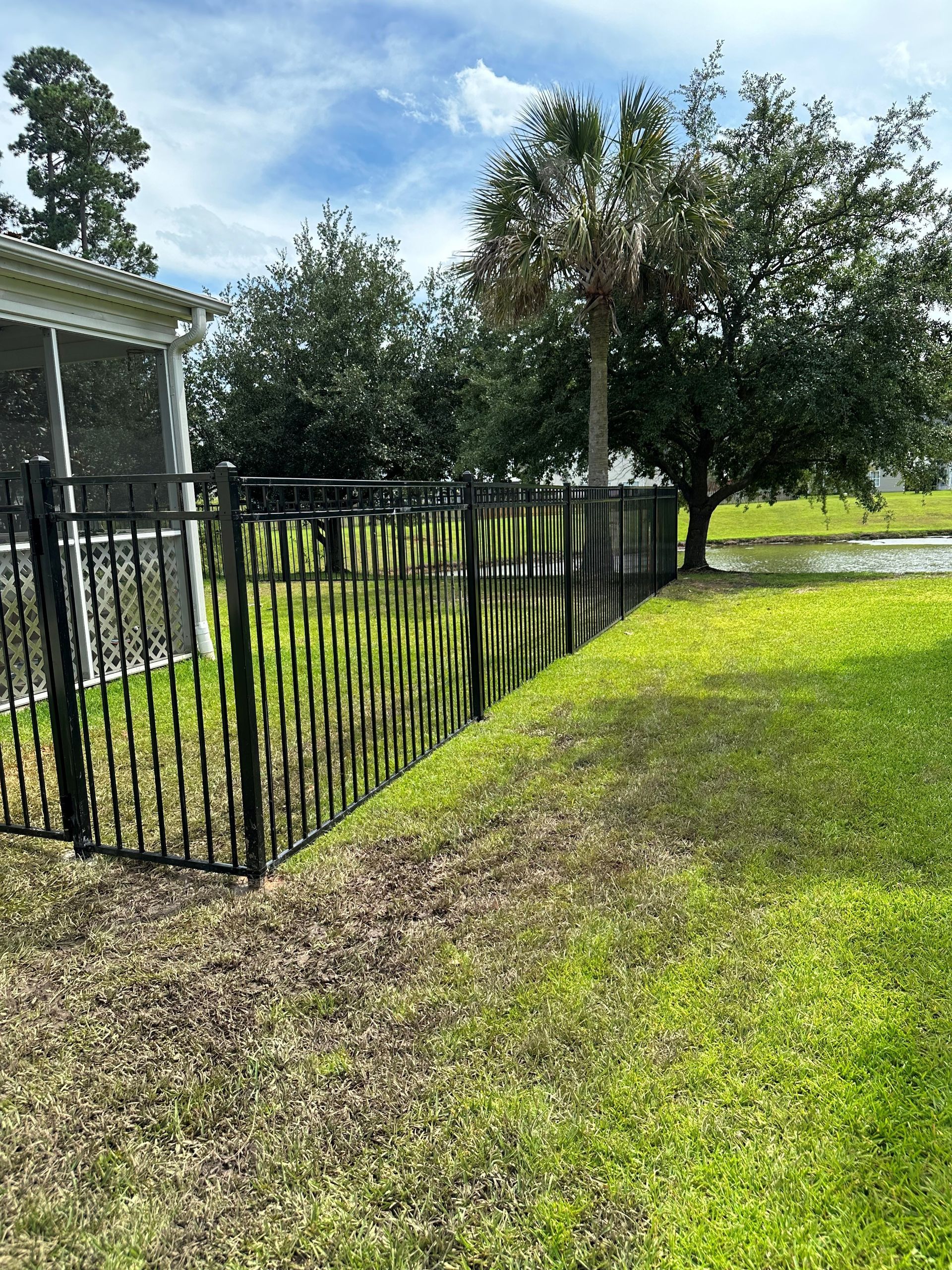Black metal fence bordering a grassy lawn with trees in the background under a cloudy sky.