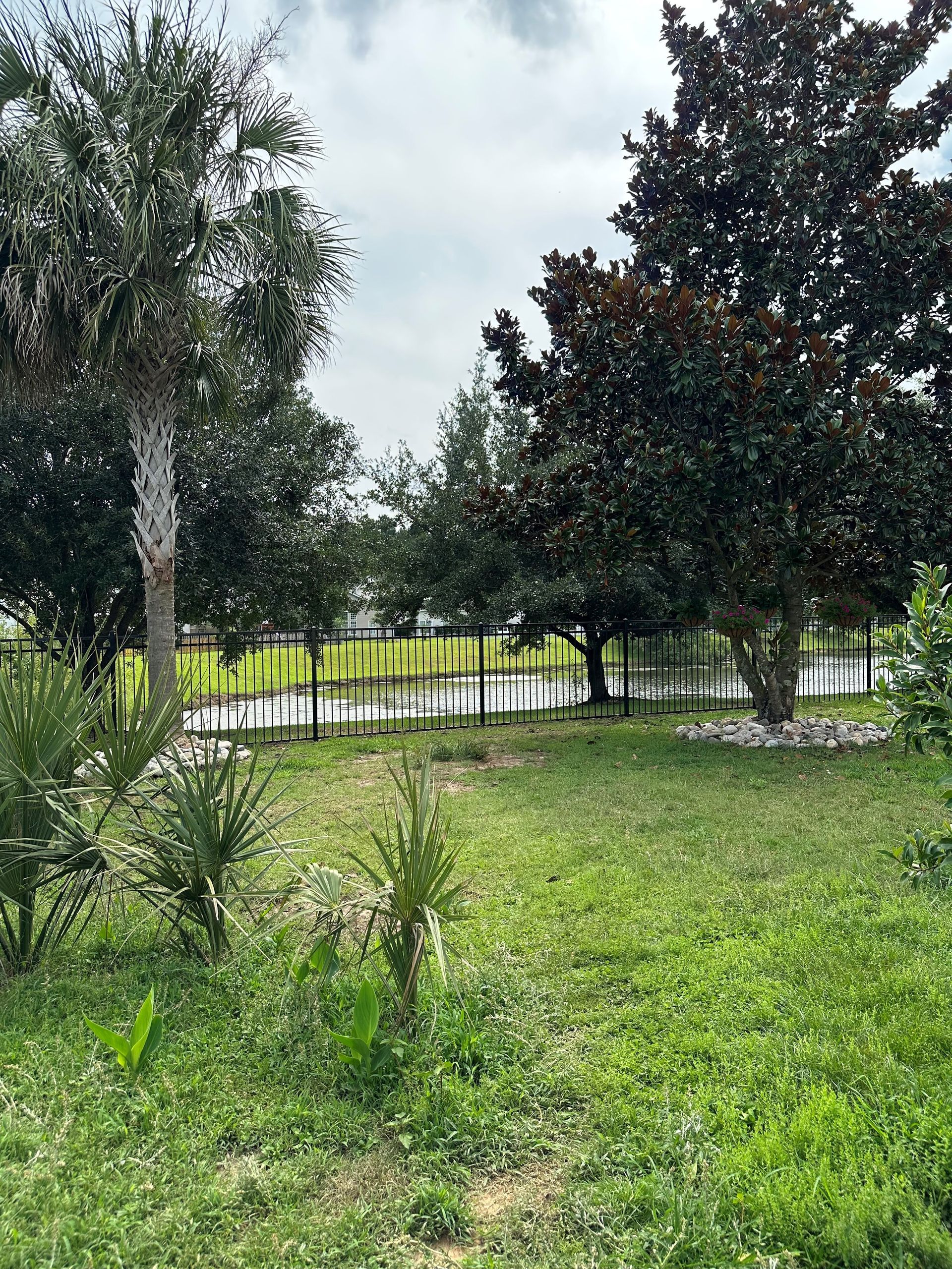 Green lawn with trees and a lake in the background under a cloudy sky.