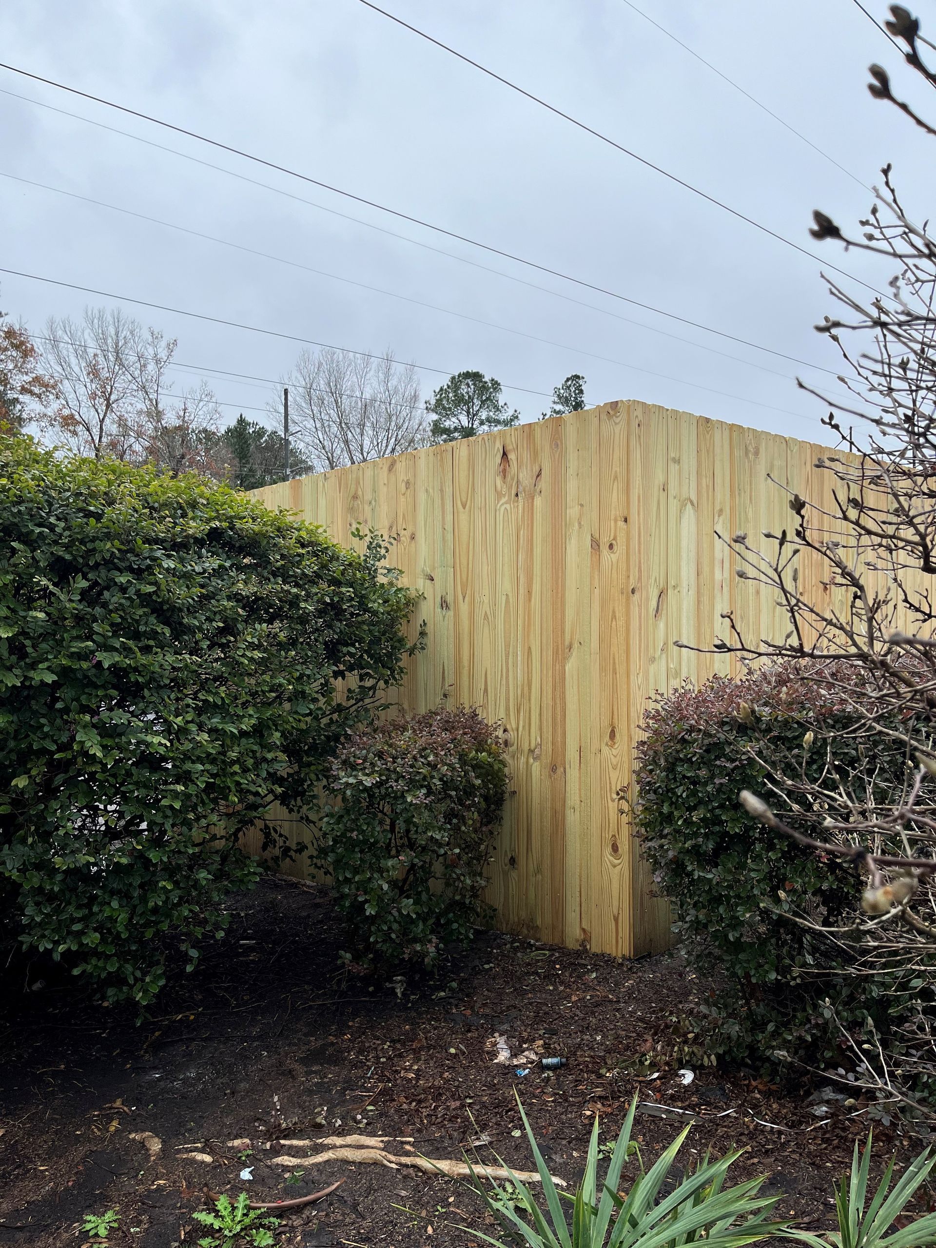 Wooden fence corner in a yard with bushes. Overcast sky.