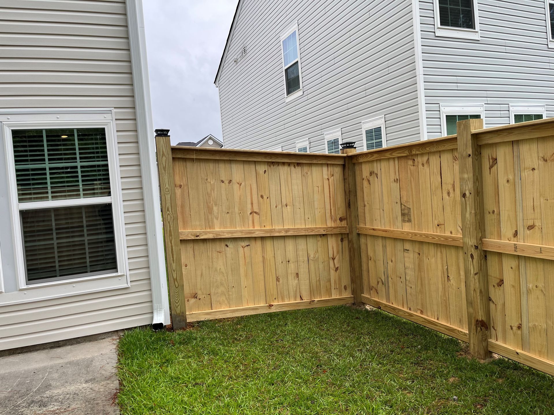Wooden fence enclosing a small grassy yard between two houses with siding.