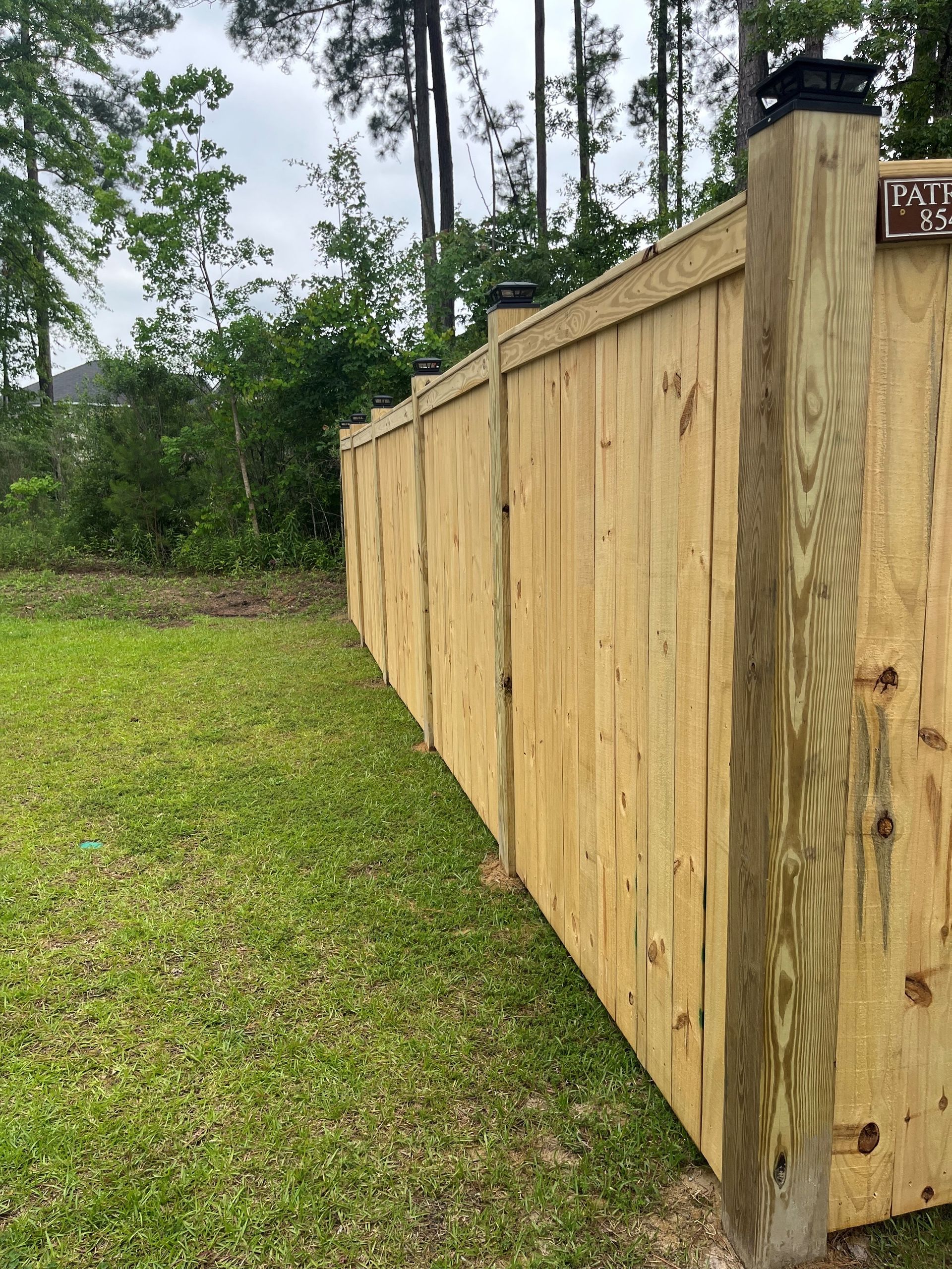 Wooden fence bordering a grassy yard, under a cloudy sky.