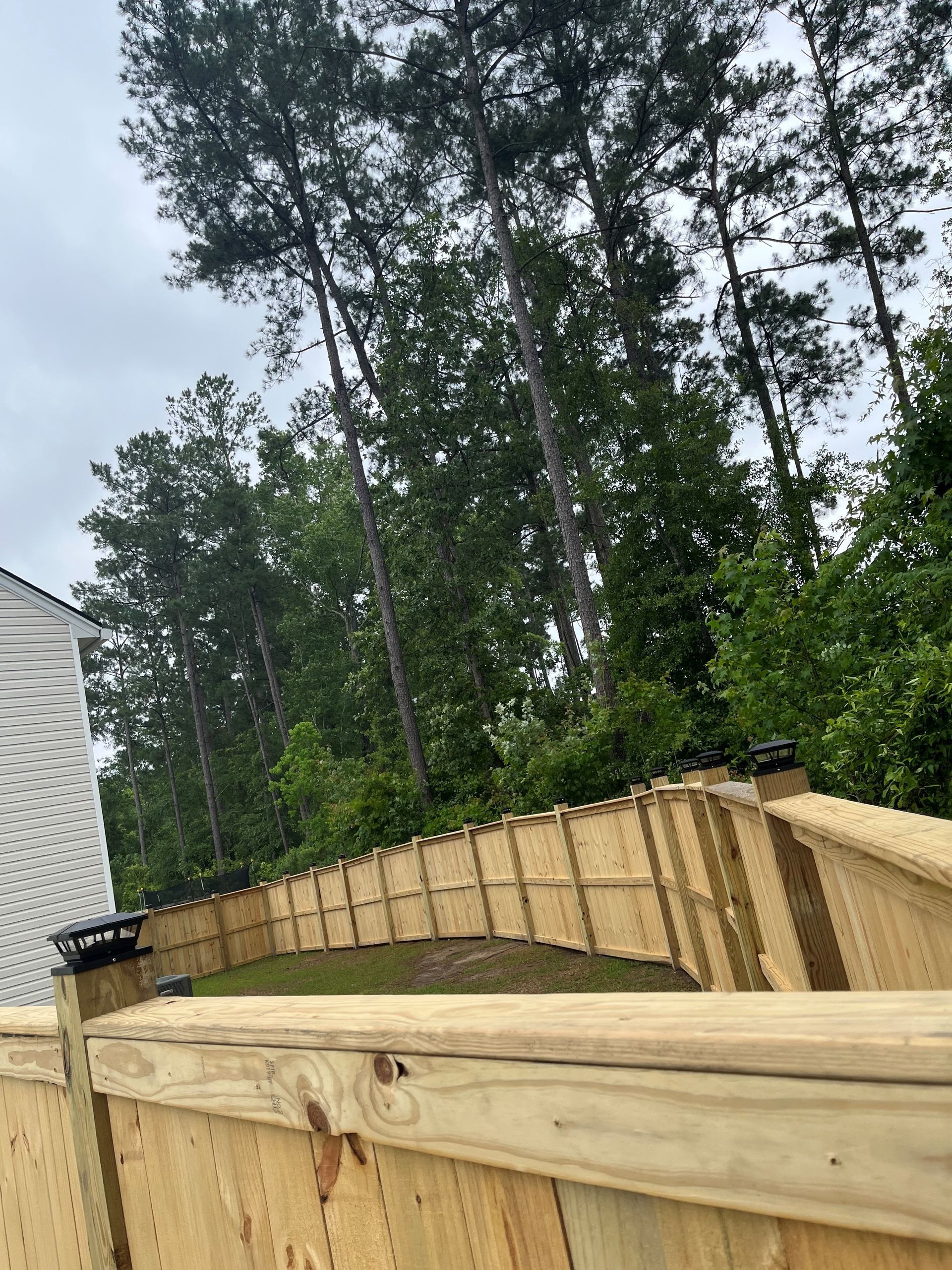 Wooden fence curving uphill with trees in the background under a cloudy sky.