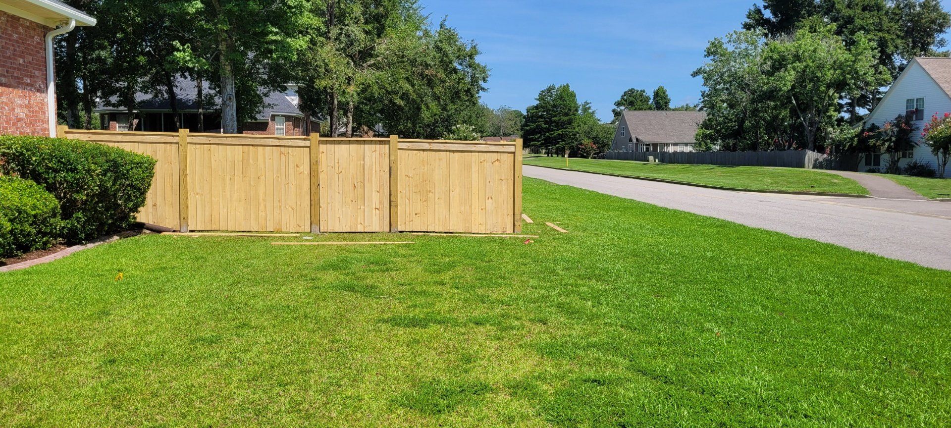 Lush green lawn with a wooden fence and houses in the background on a sunny day.