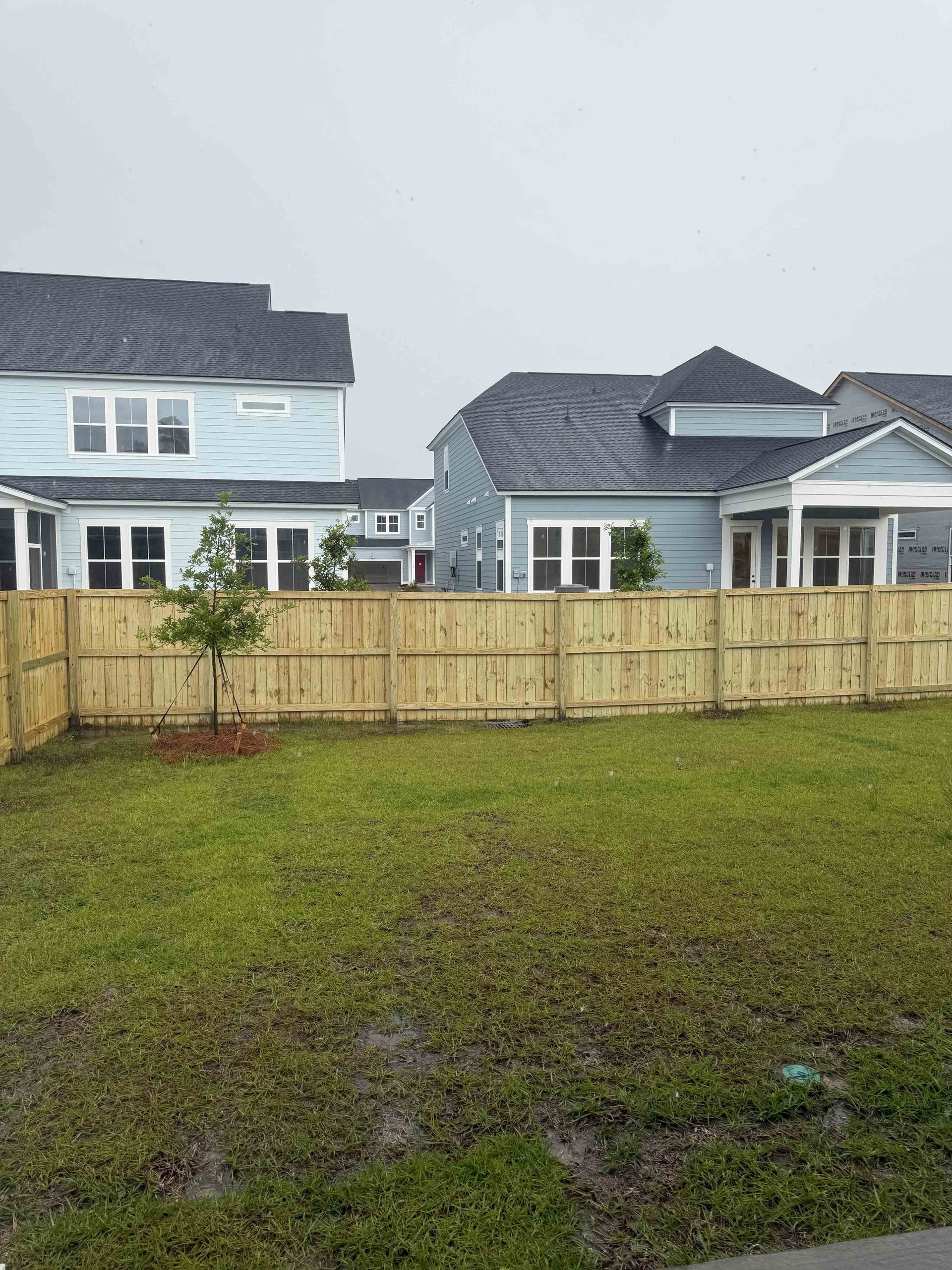 Backyard lawn with wooden fence and modern houses in the background under a gray sky