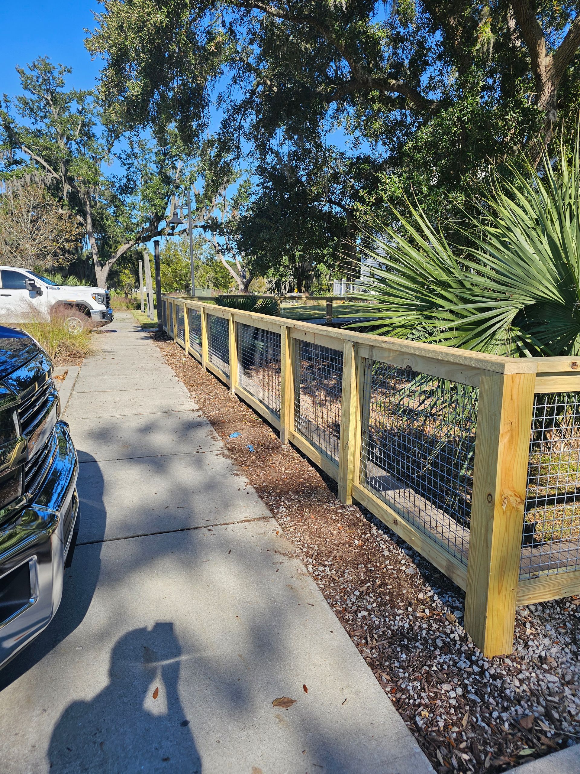 A wooden fence with black wire mesh next to a sidewalk.