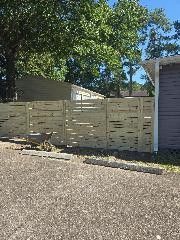 Wooden horizontal slat fence in front of a building; gravel driveway.