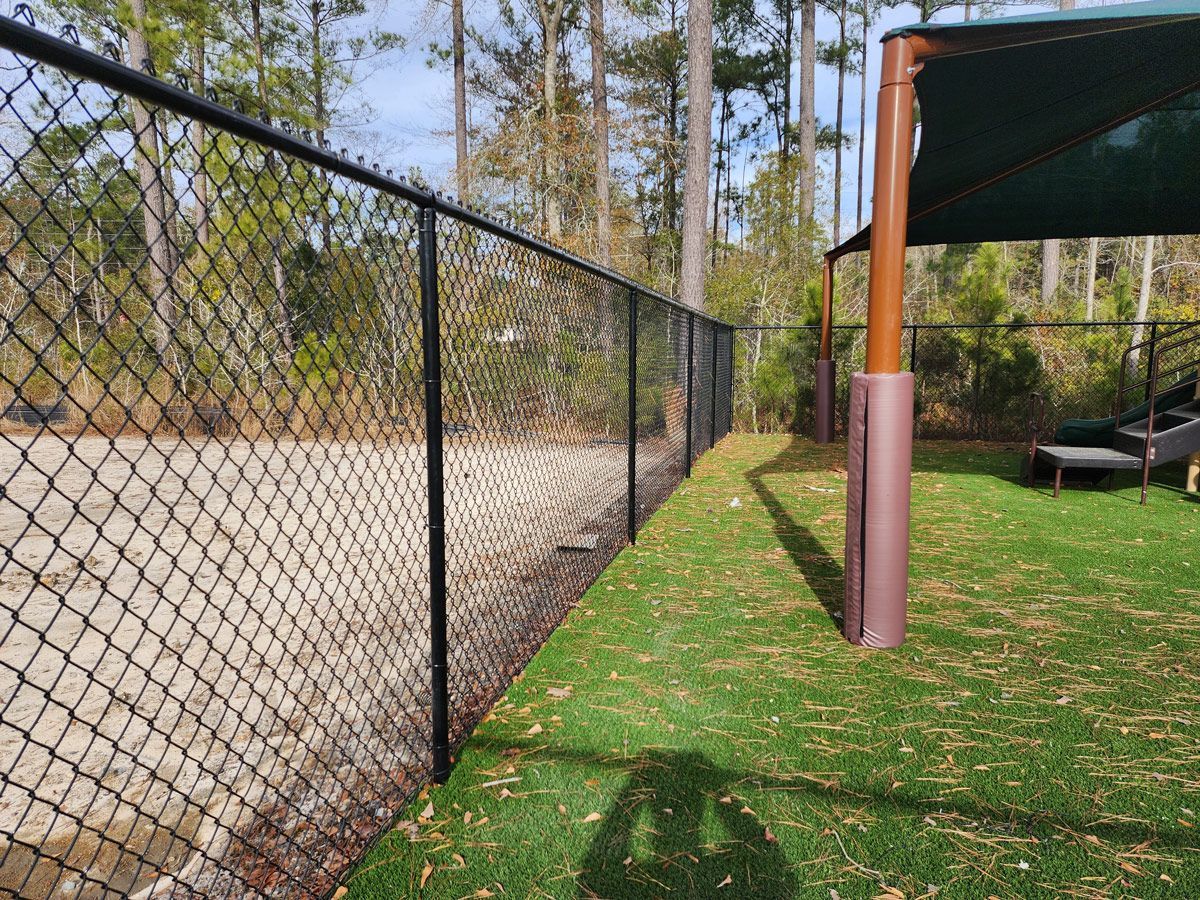 Black chain-link fence bordering a grassy area with a shaded structure, set in a natural, outdoor environment.