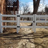 White three-rail fence with a gate, in front of a stone pathway.