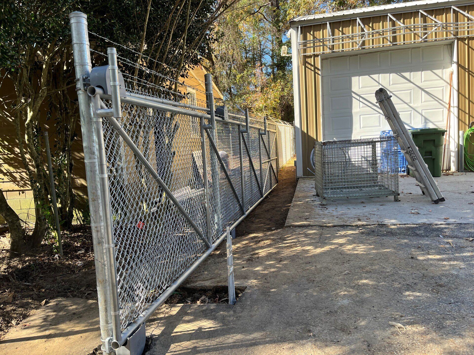 Chain-link fence with gate, gravel ground, and garage in the background.