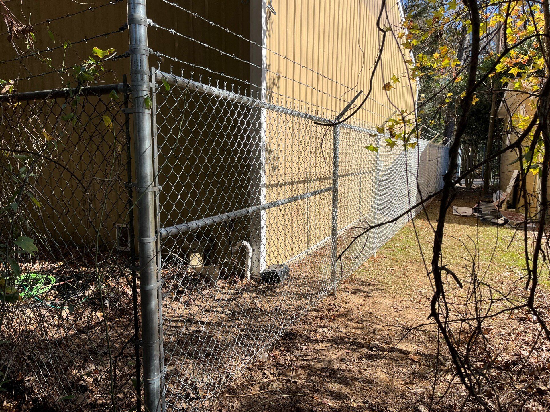 Chain-link fence next to a yellow building and fallen leaves on the ground.