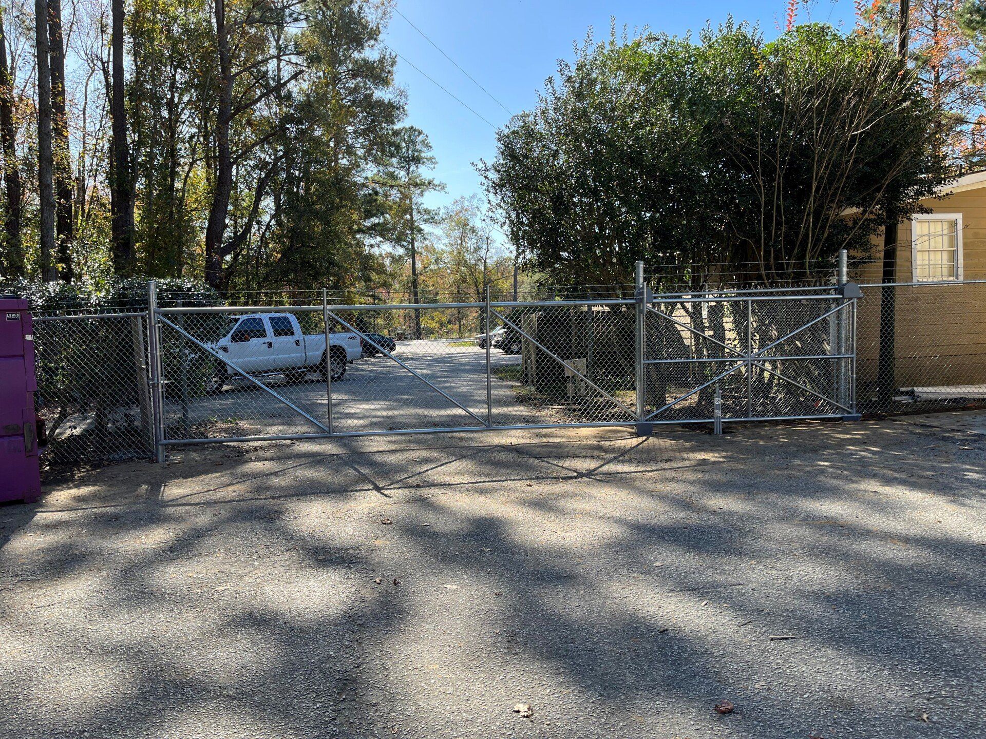 Gravel driveway with chain link gate. A white pickup truck is parked behind the gate.