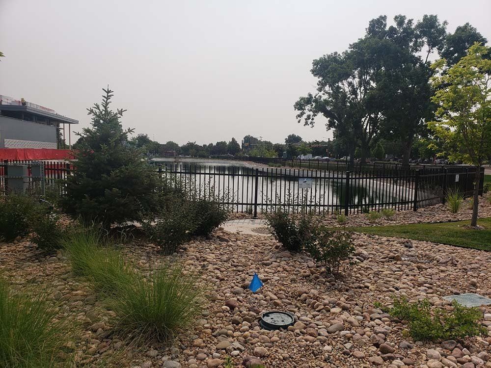 Pond surrounded by black metal fence and landscaping, under a hazy sky.