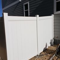 White vinyl fence along the side of a building with a window, set on gravel.
