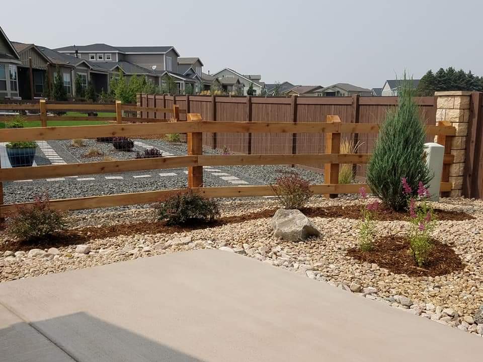 Wooden fence and landscaping border a concrete patio in a residential yard.