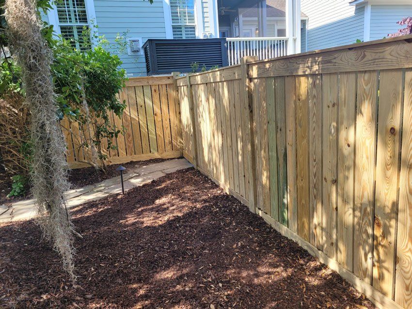Wooden fence bordering a yard covered in mulch. A tree hangs on the left.