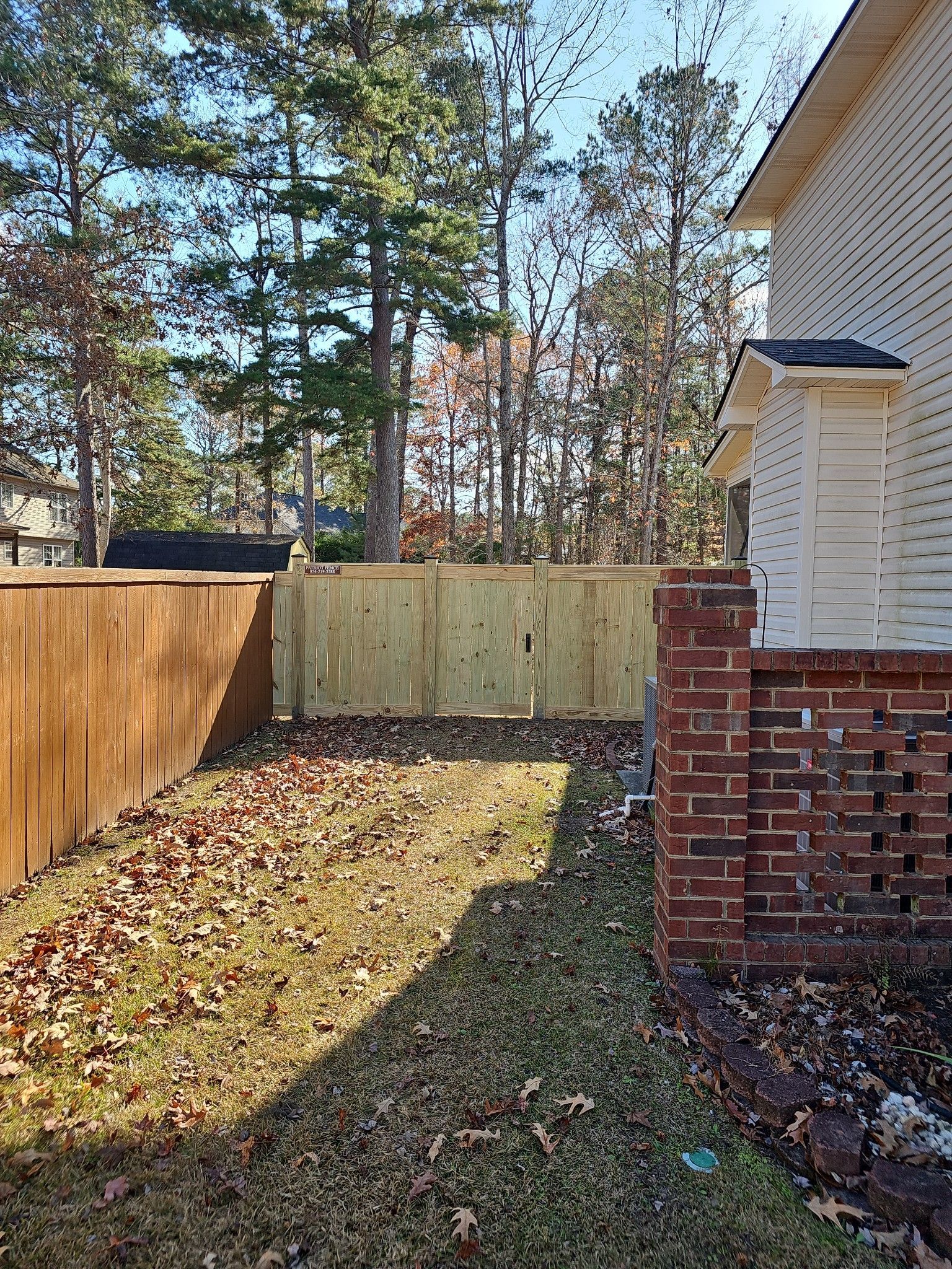 Backyard with brown and light wood fences, brickwork, and fallen leaves on the grass.