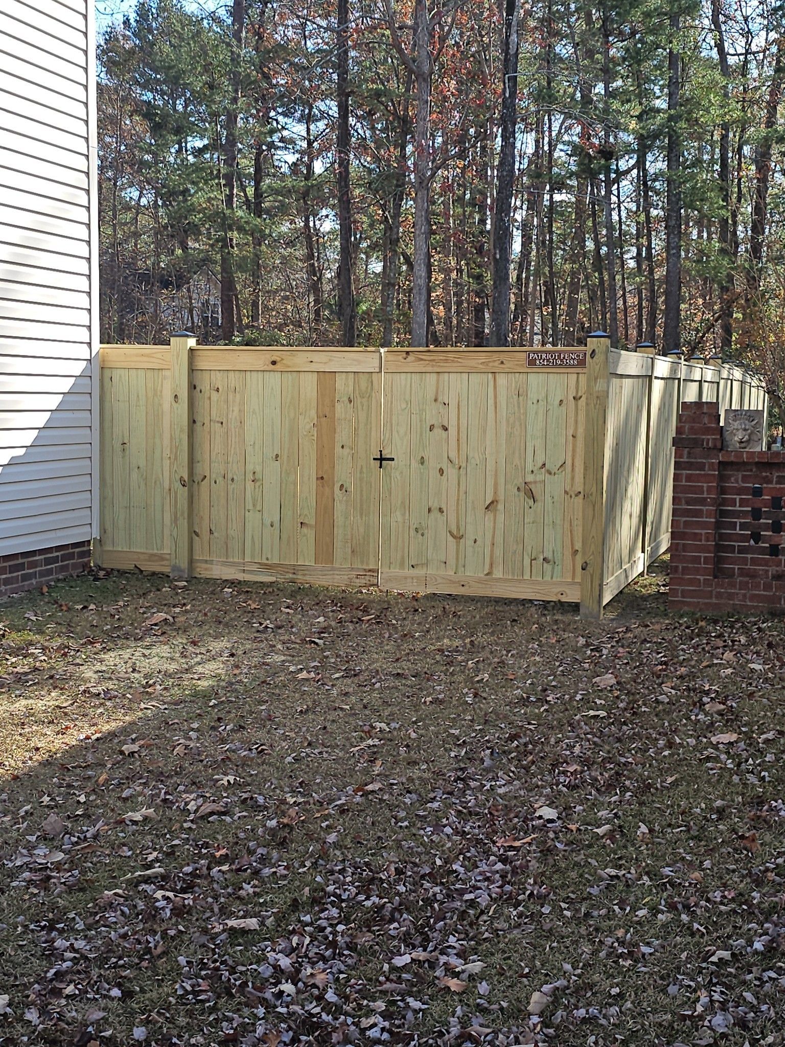 Wooden privacy fence in a backyard, with a brick structure on the right, trees in the background.