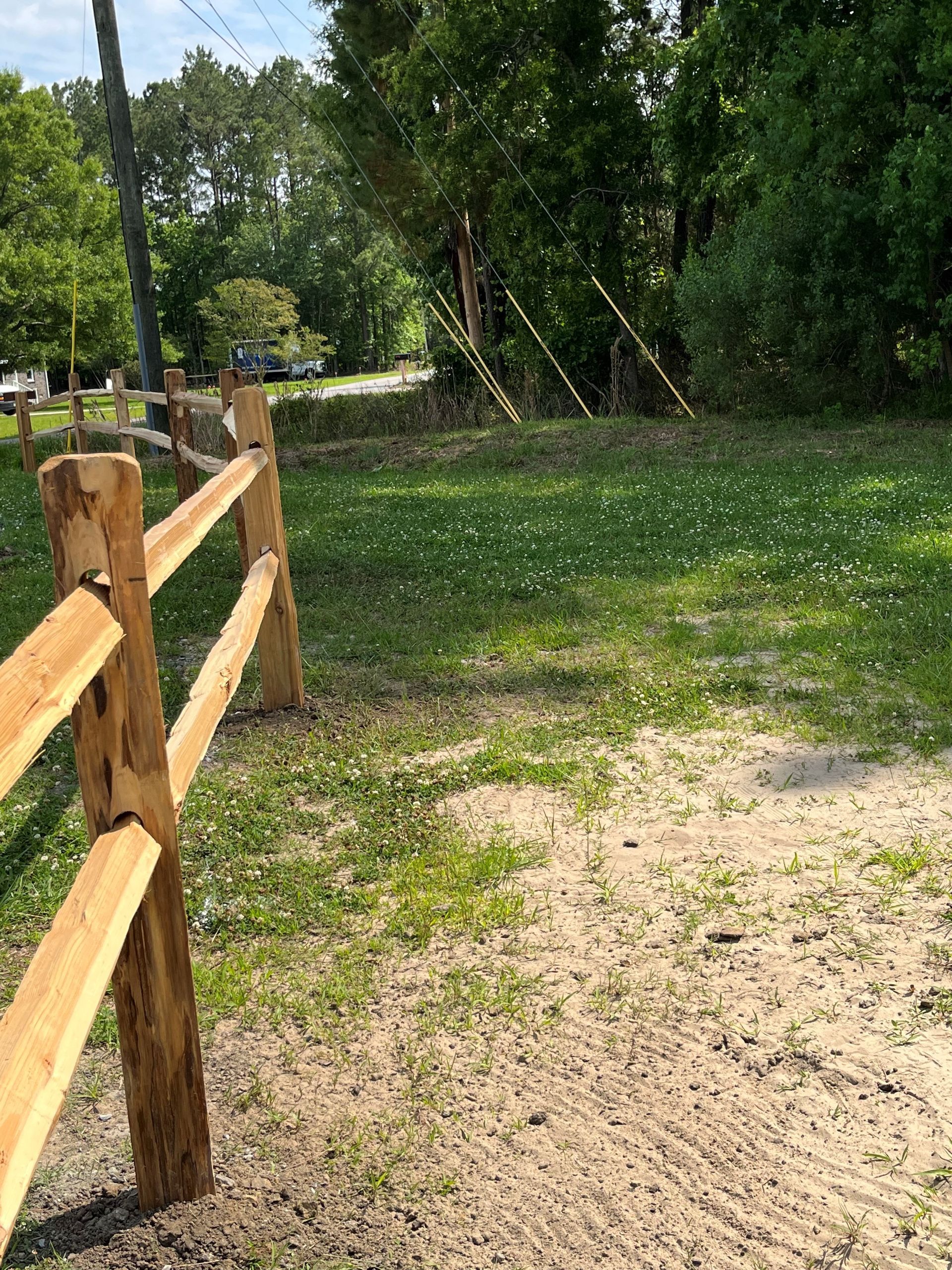 Wooden fence frames a grassy area near trees and a road.